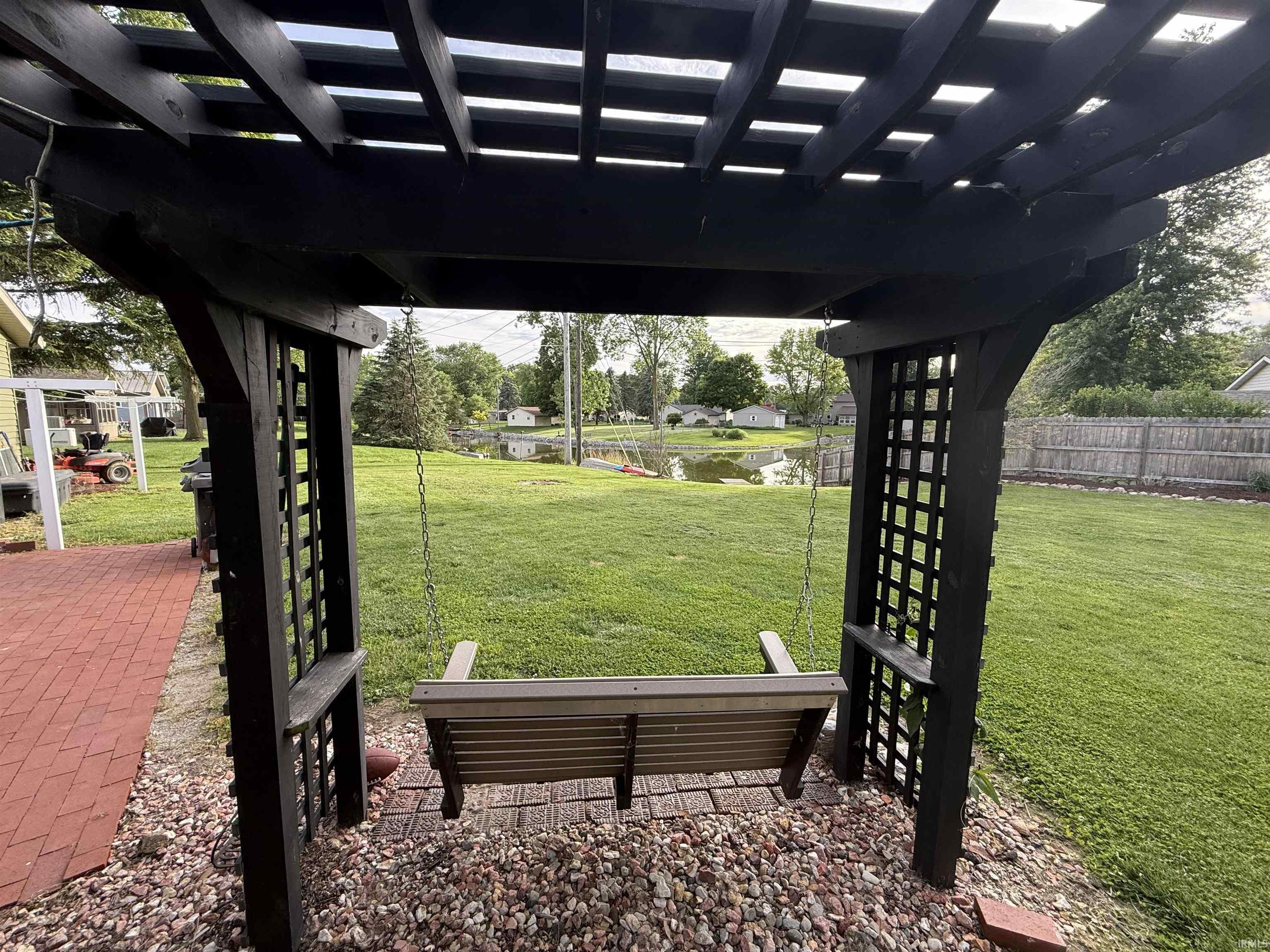 Backyard pergola with a wooden swing, red brick patio, and gravel landscaping