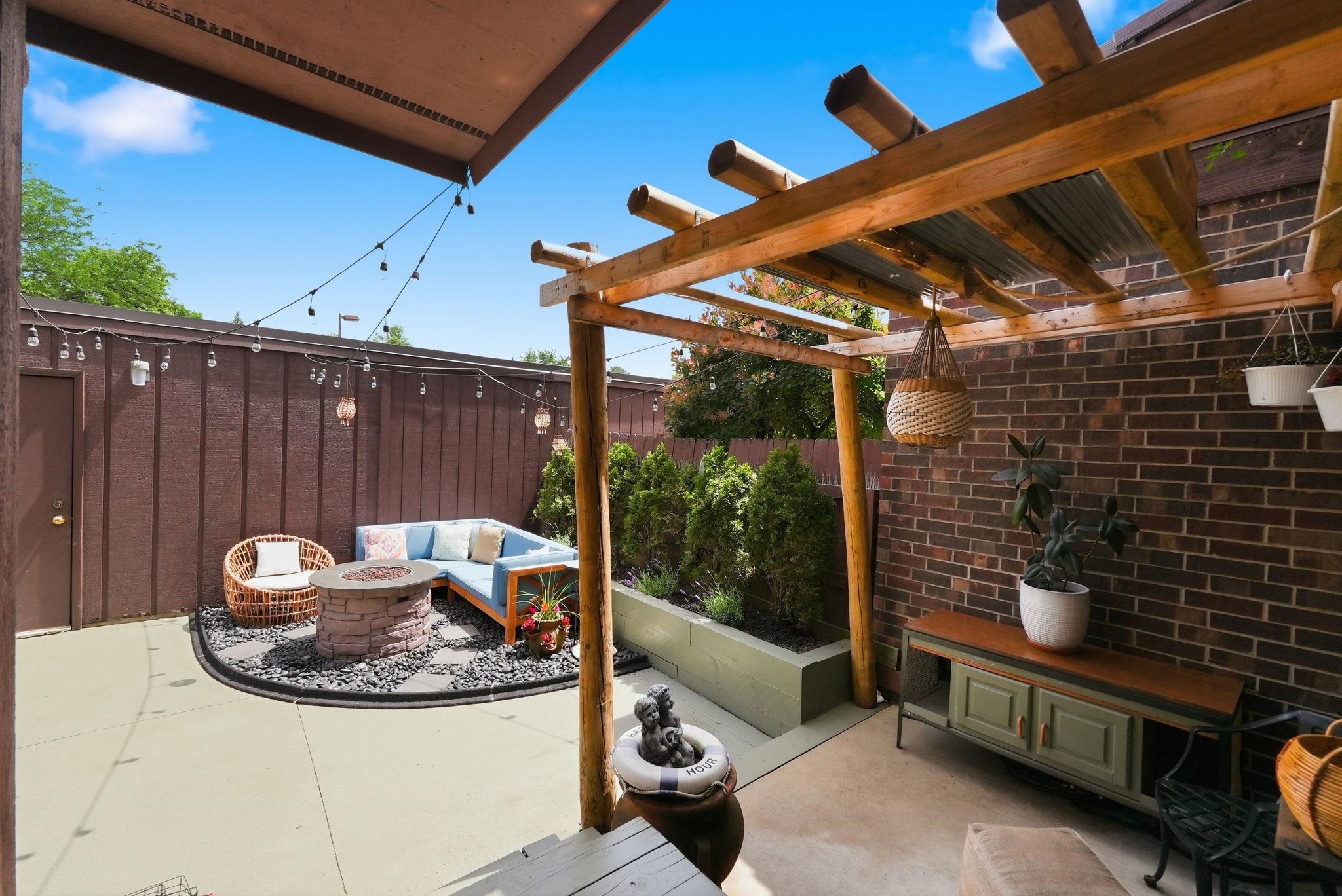 Private patio featuring a stone fire pit, concrete flooring, and a pergola with corrugated metal roofing