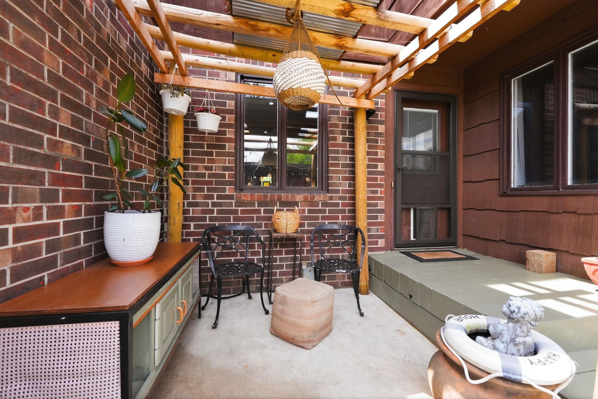Outdoor patio area featuring a slatted wood pergola, brick exterior, and a built-in wood-top console