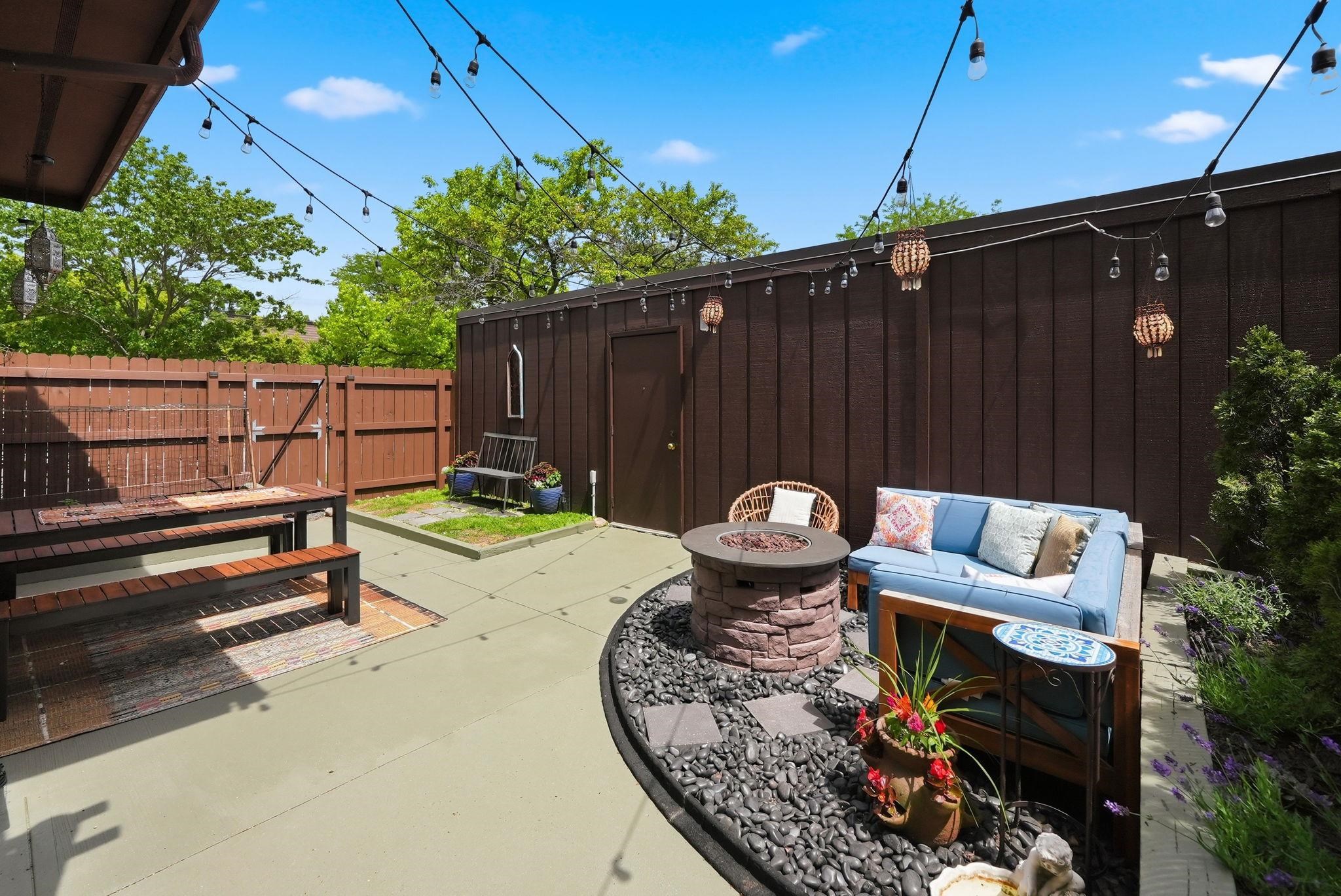 Spacious outdoor patio featuring concrete paving, a fire pit area with black river rock, and a privacy fence