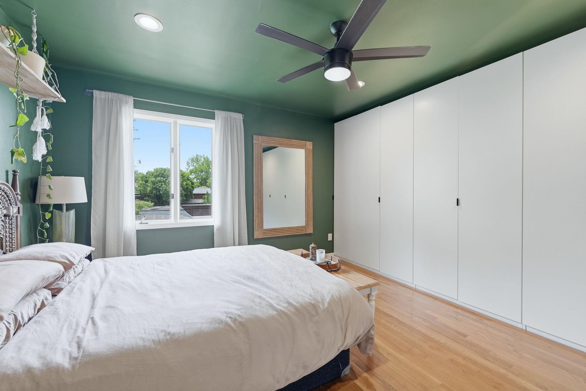 Built-in wardrobe system with sleek white doors, wood-finish flooring, recessed lighting, and a modern ceiling fan