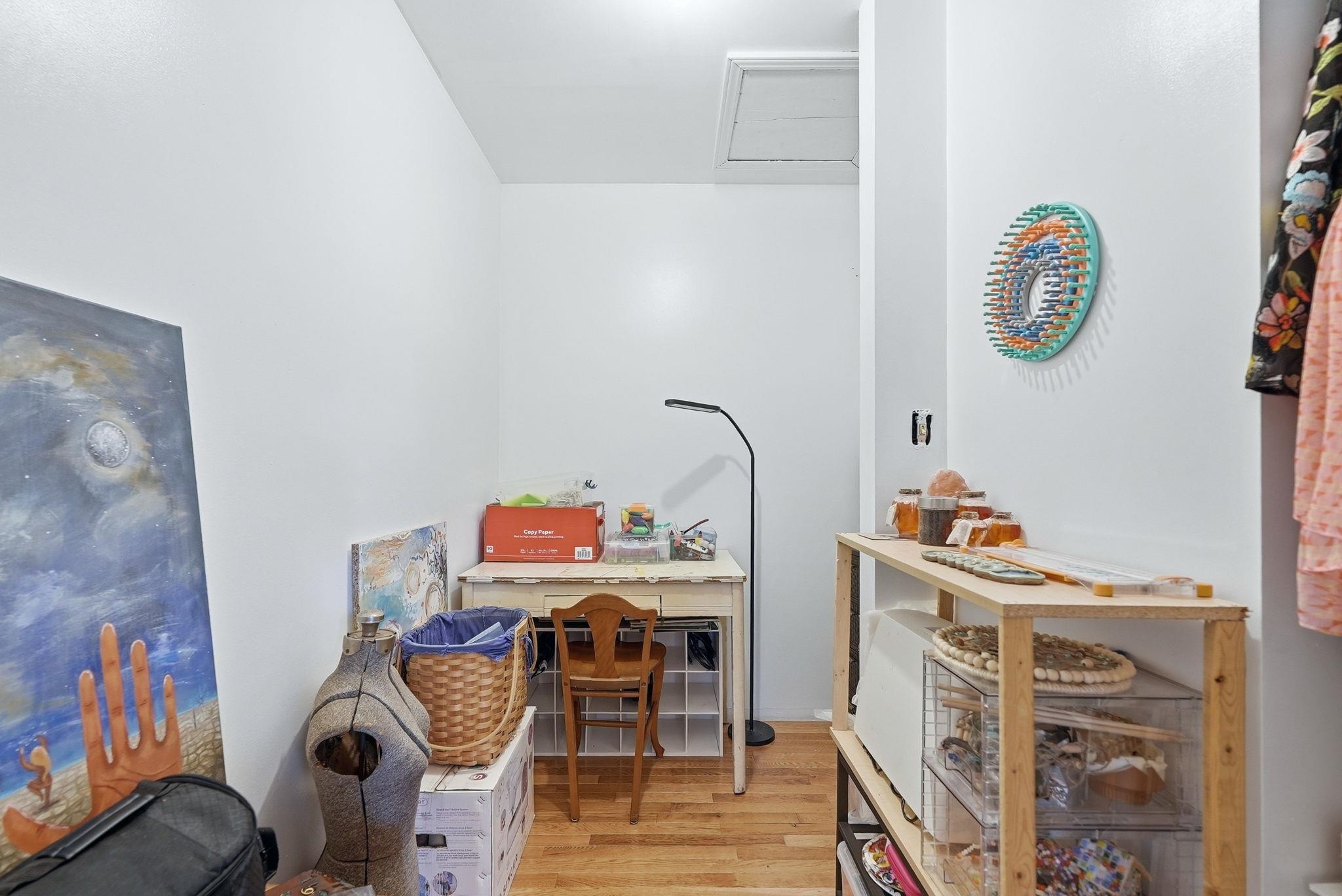 Hardwood-finish flooring extending throughout, white painted walls, and a visible attic access panel