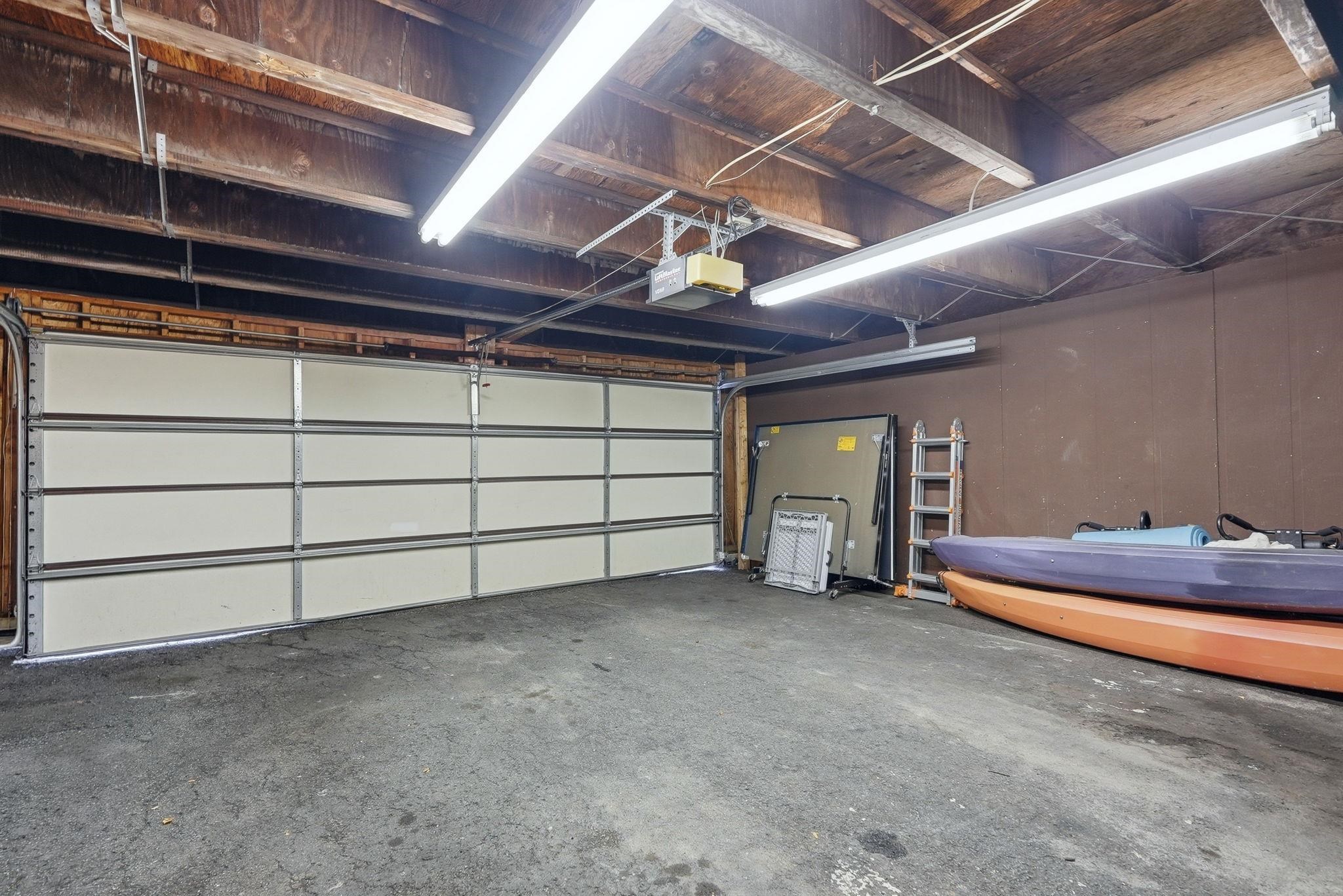 Attached garage featuring a segmented overhead door, exposed wood beam ceiling, and concrete flooring