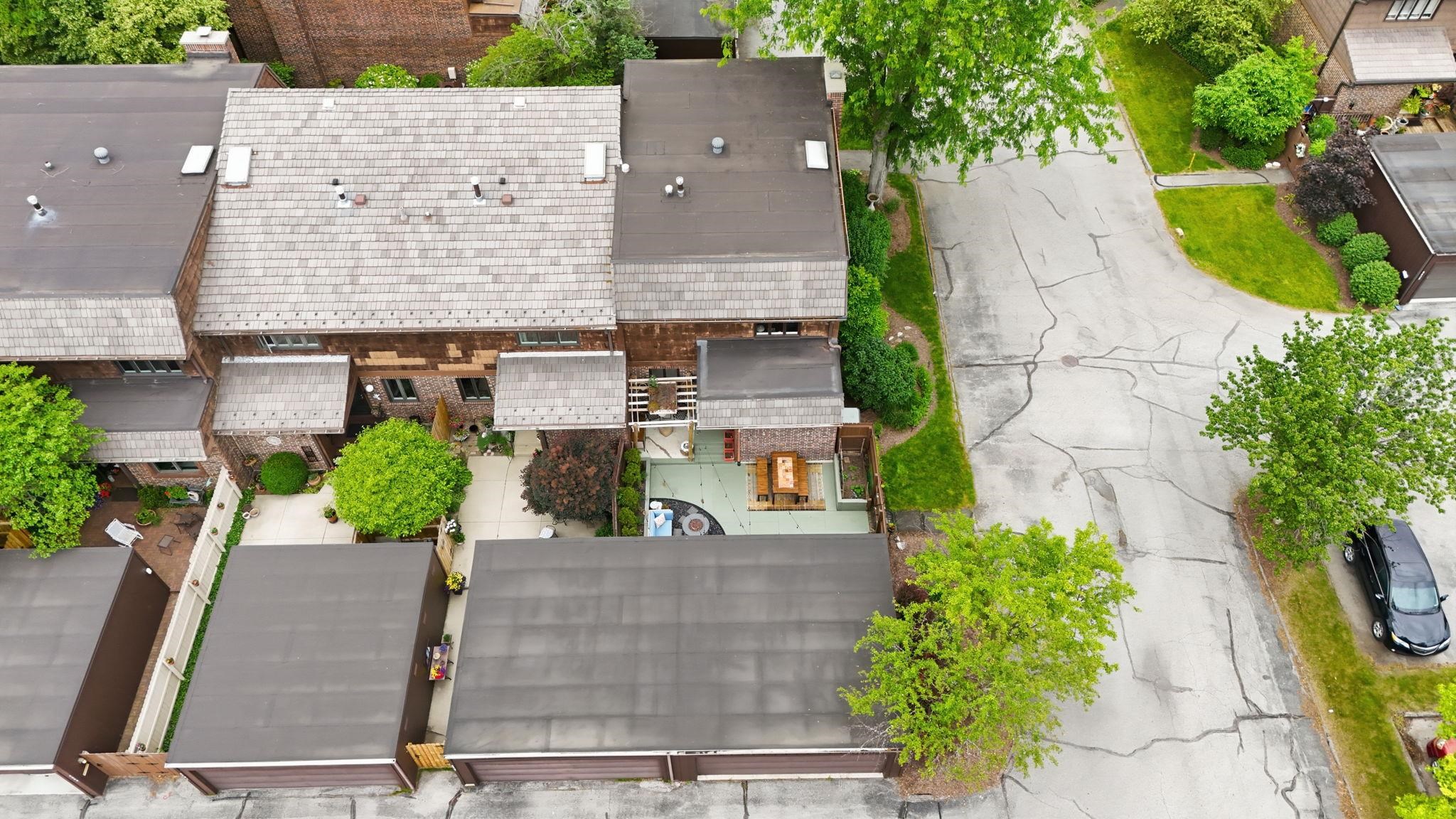 Townhouse exterior featuring a shingle roof, wood siding, and mature landscaping
