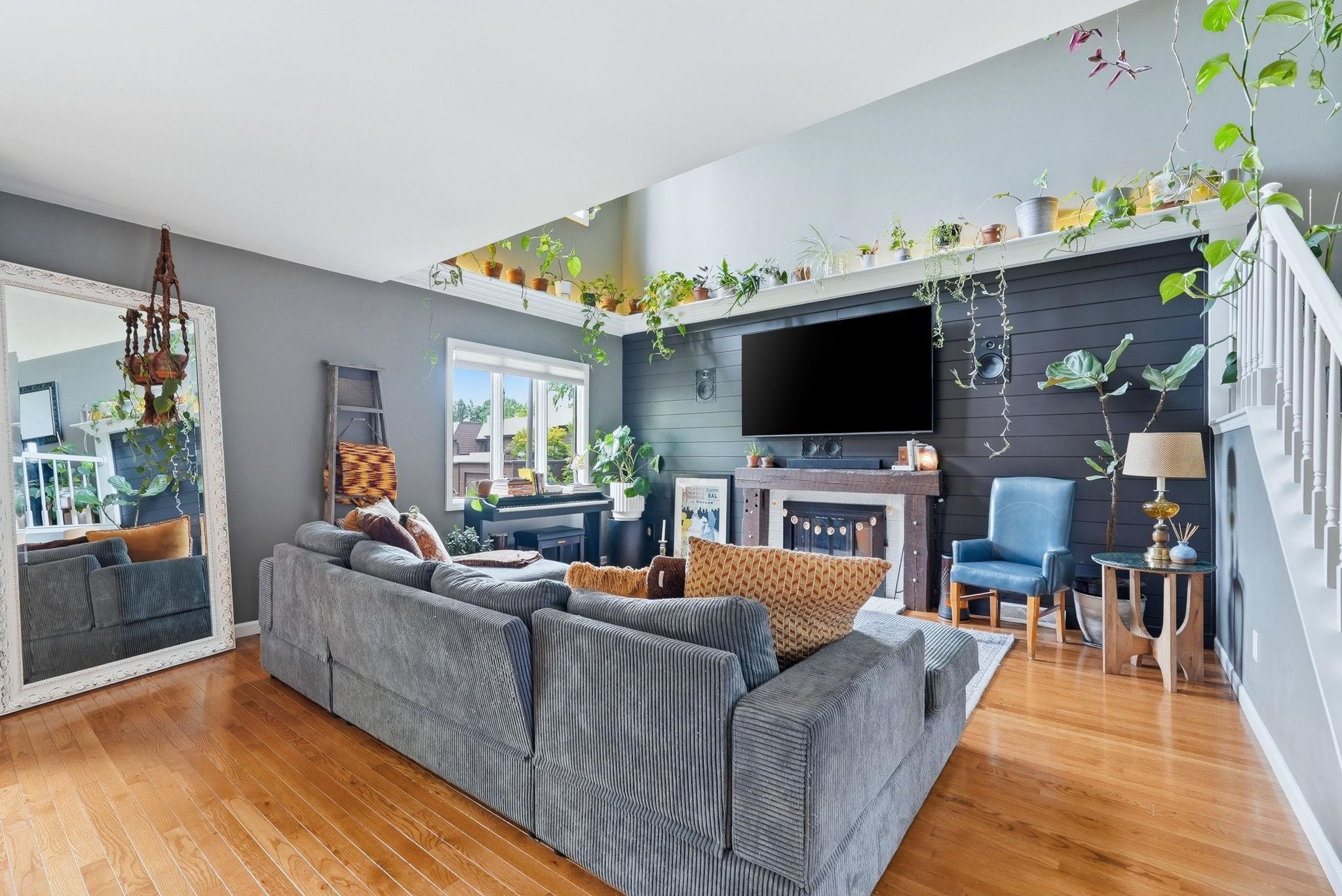 Living area featuring wood-finish flooring, a fireplace with a mantel, a wall-mounted television, and a window with natural light