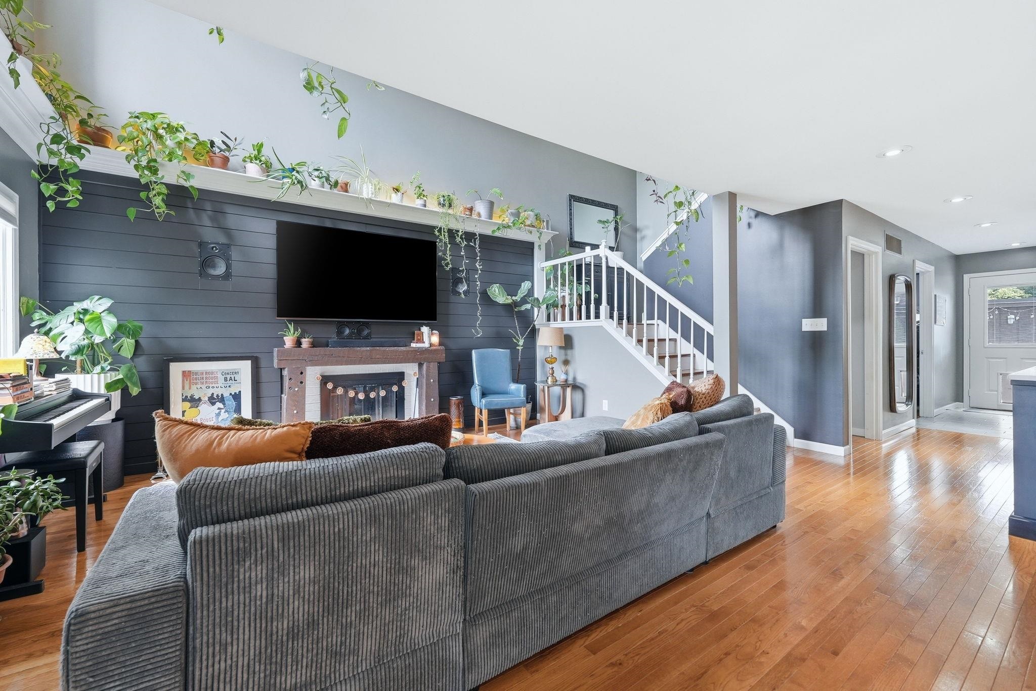 Open concept living area featuring wood-finish flooring, a fireplace with a wood mantle, and a prominent staircase with white railings