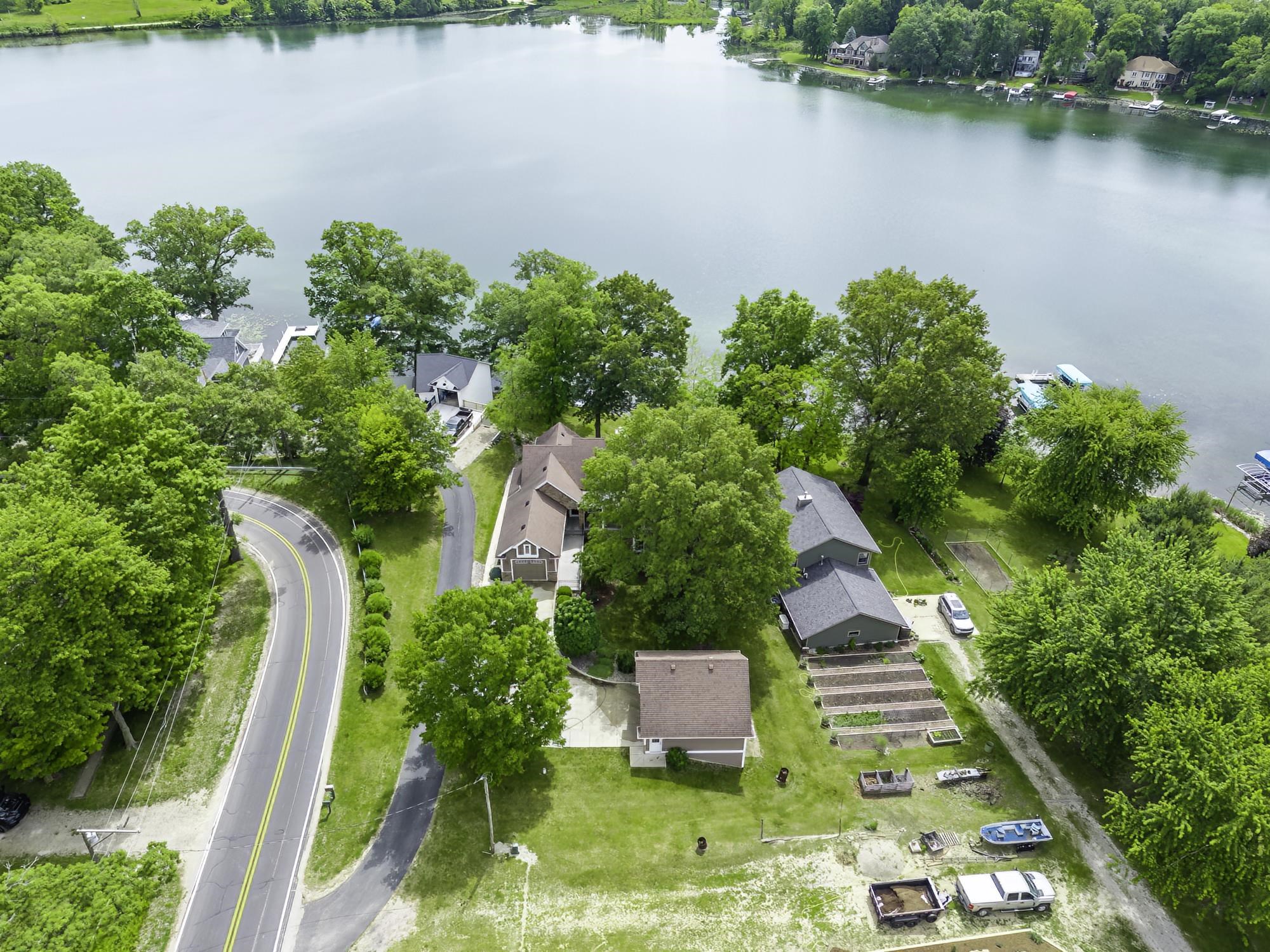 Expansive lakefront property featuring a primary residence with a dark gray shingle roof, a secondary structure with a light brown shingle roof, and a terraced garden area