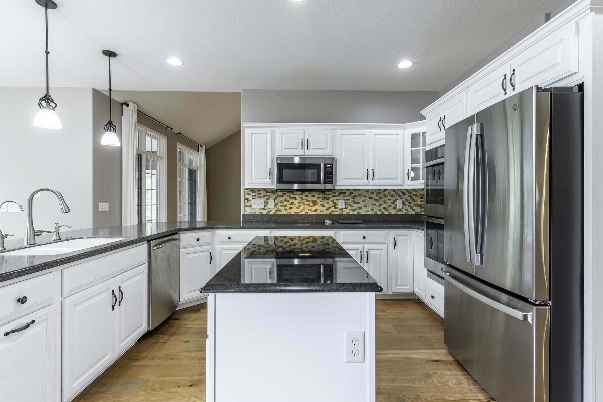 Kitchen featuring white cabinetry, dark stone countertops, stainless steel appliances, a mosaic tile backsplash, and wood-finish flooring