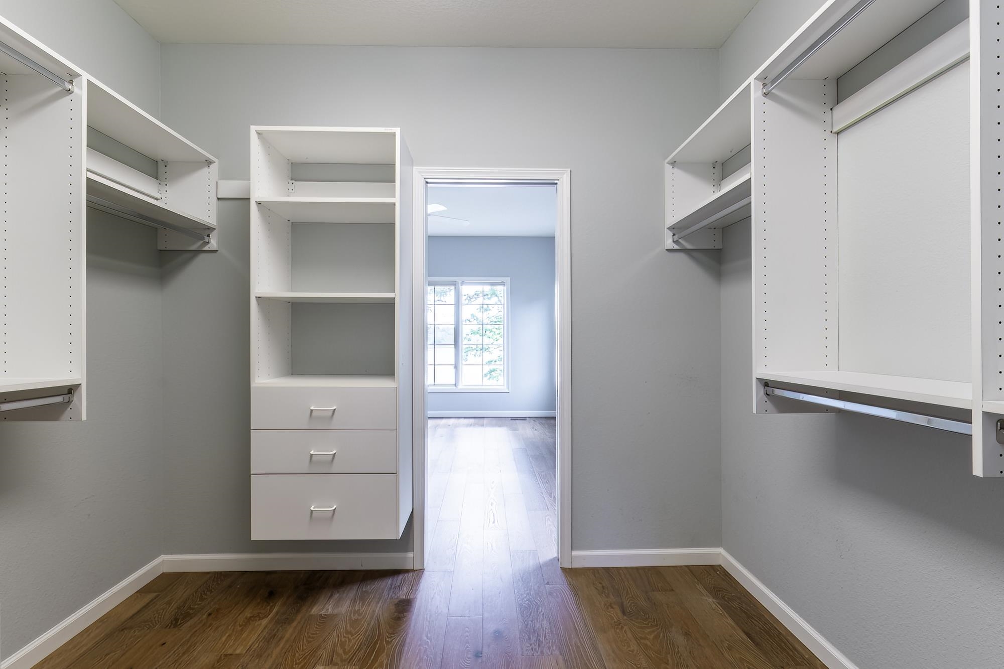Walk-in closet featuring wood-finish flooring, light gray walls, built-in shelving, integrated hanging rods, and three white drawers with metal pulls