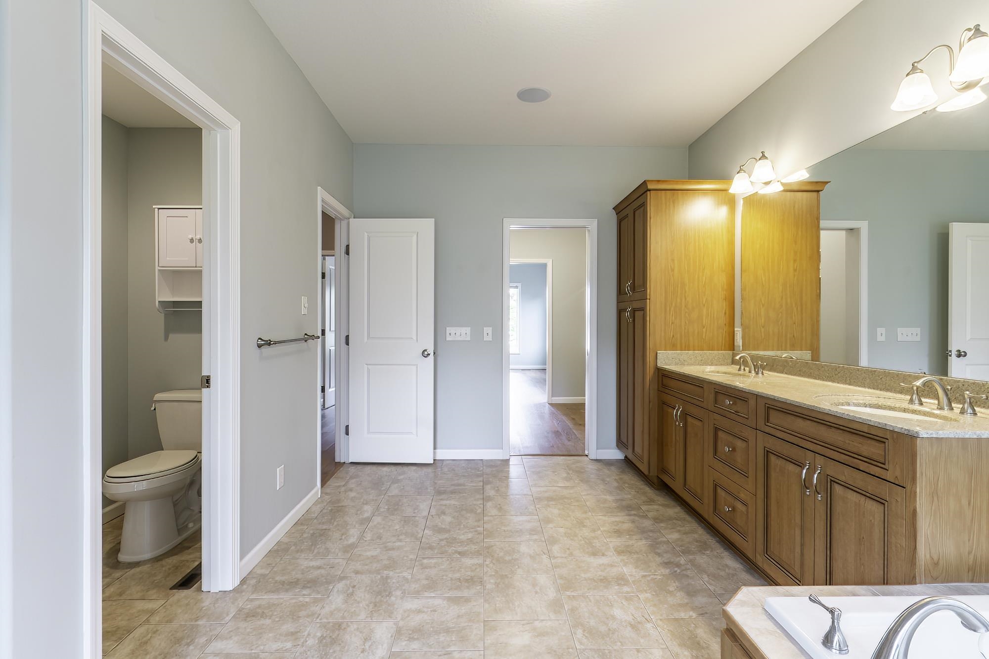 Bathroom featuring a double vanity with stone countertops, wood cabinetry, tile flooring, and a separate water closet