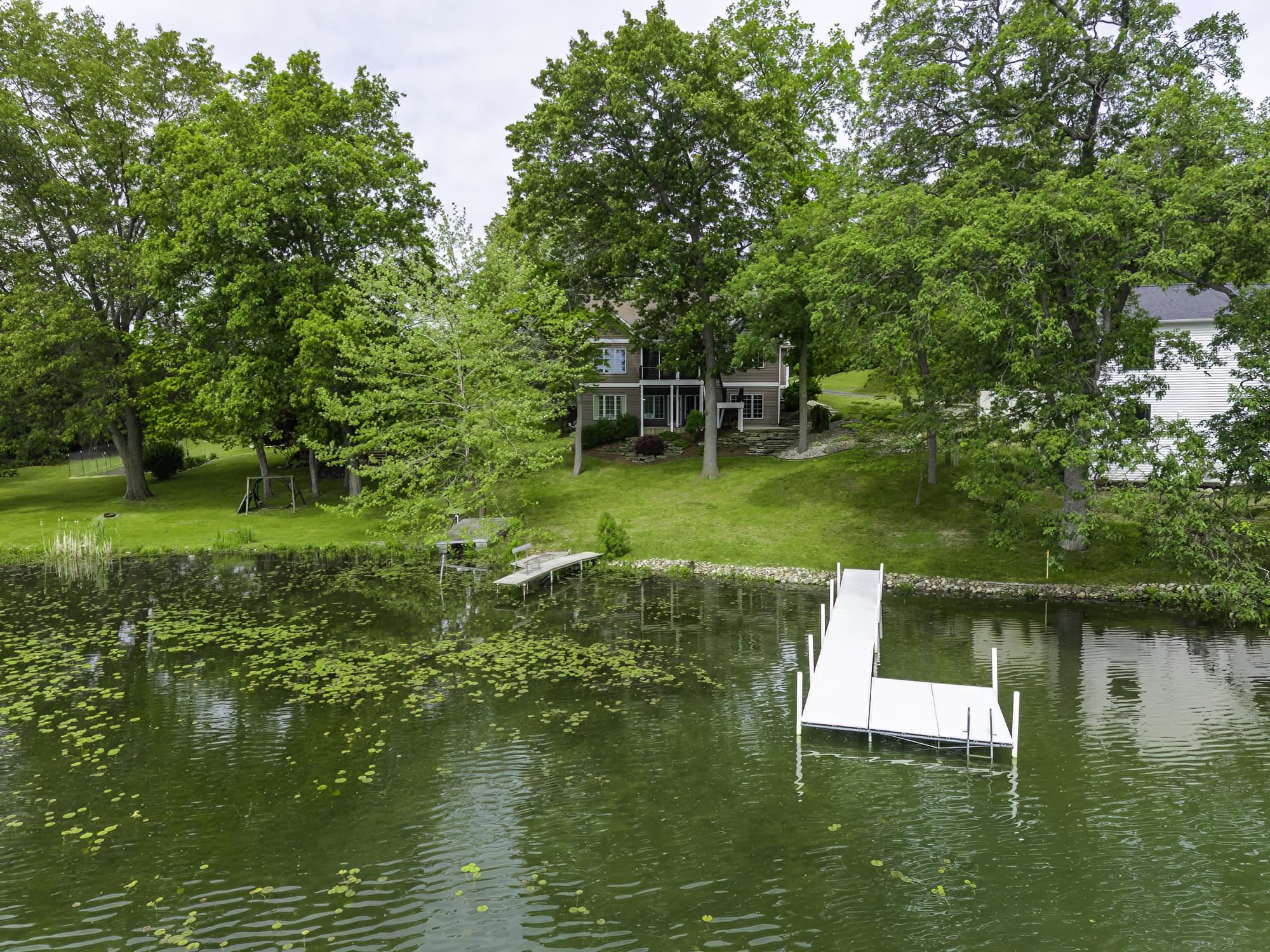 L-shaped dock on a green-tinted body of water with lily pads, backed by a lush green lawn and mature trees