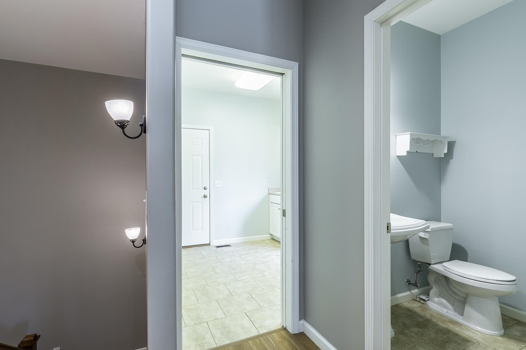 Hallway featuring light gray walls, white trim, and wall-mounted sconces