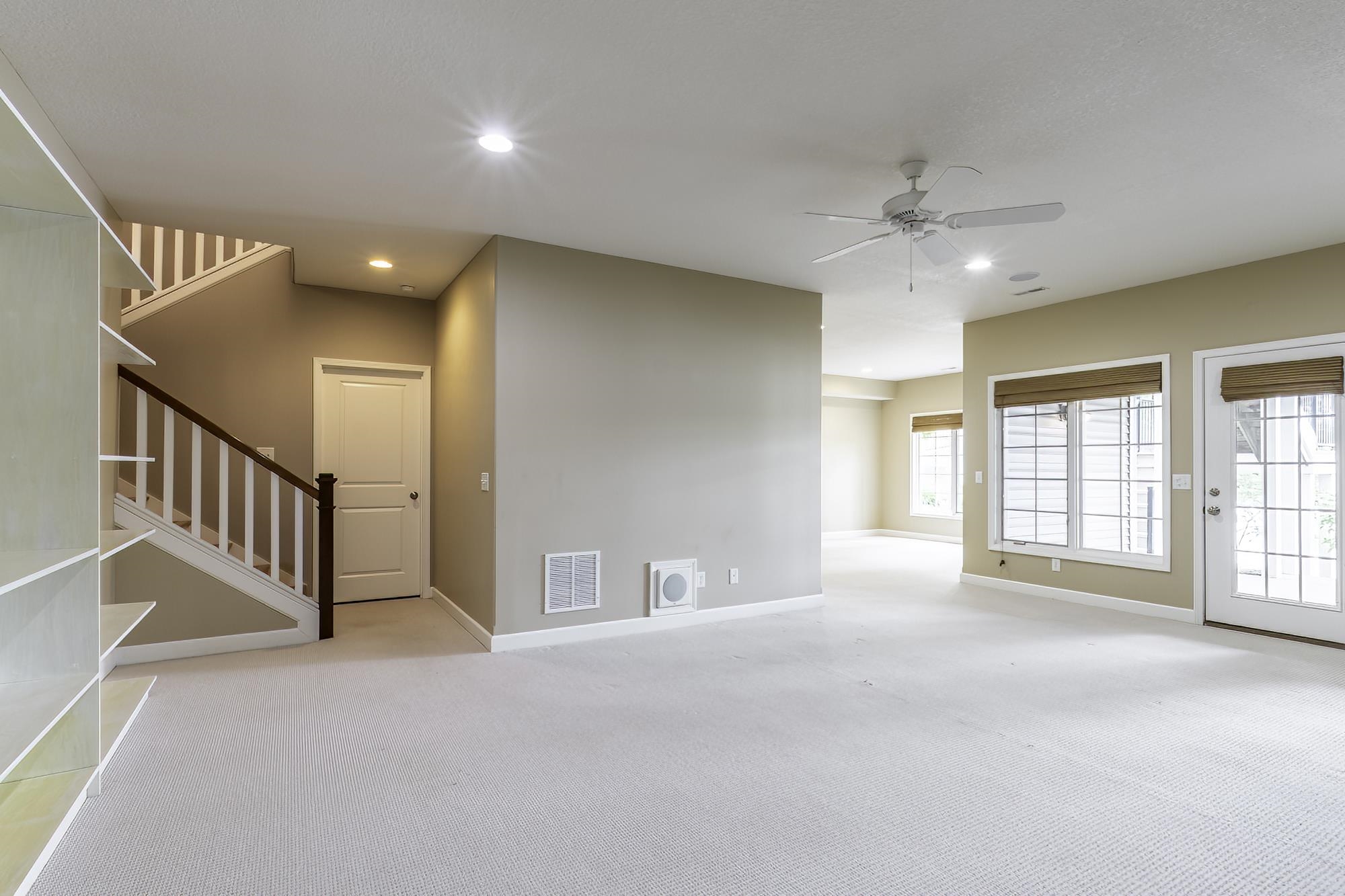 Spacious area featuring neutral carpeting, a staircase with dark wood railing, and built-in shelving
