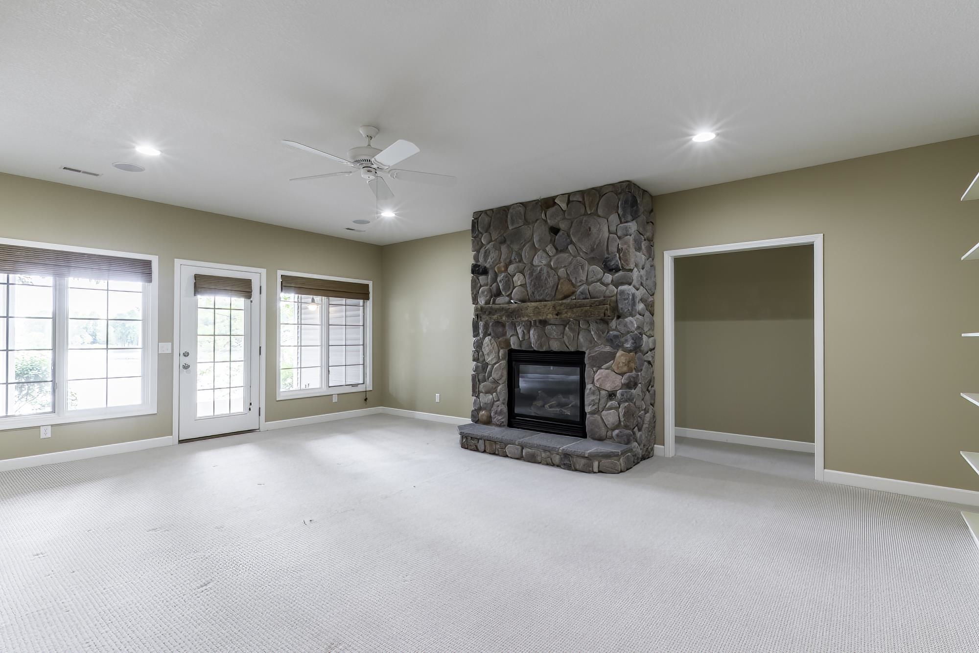 Living space featuring a stone-clad fireplace with a wood mantel, a ceiling fan, recessed lighting, and light-colored carpeting