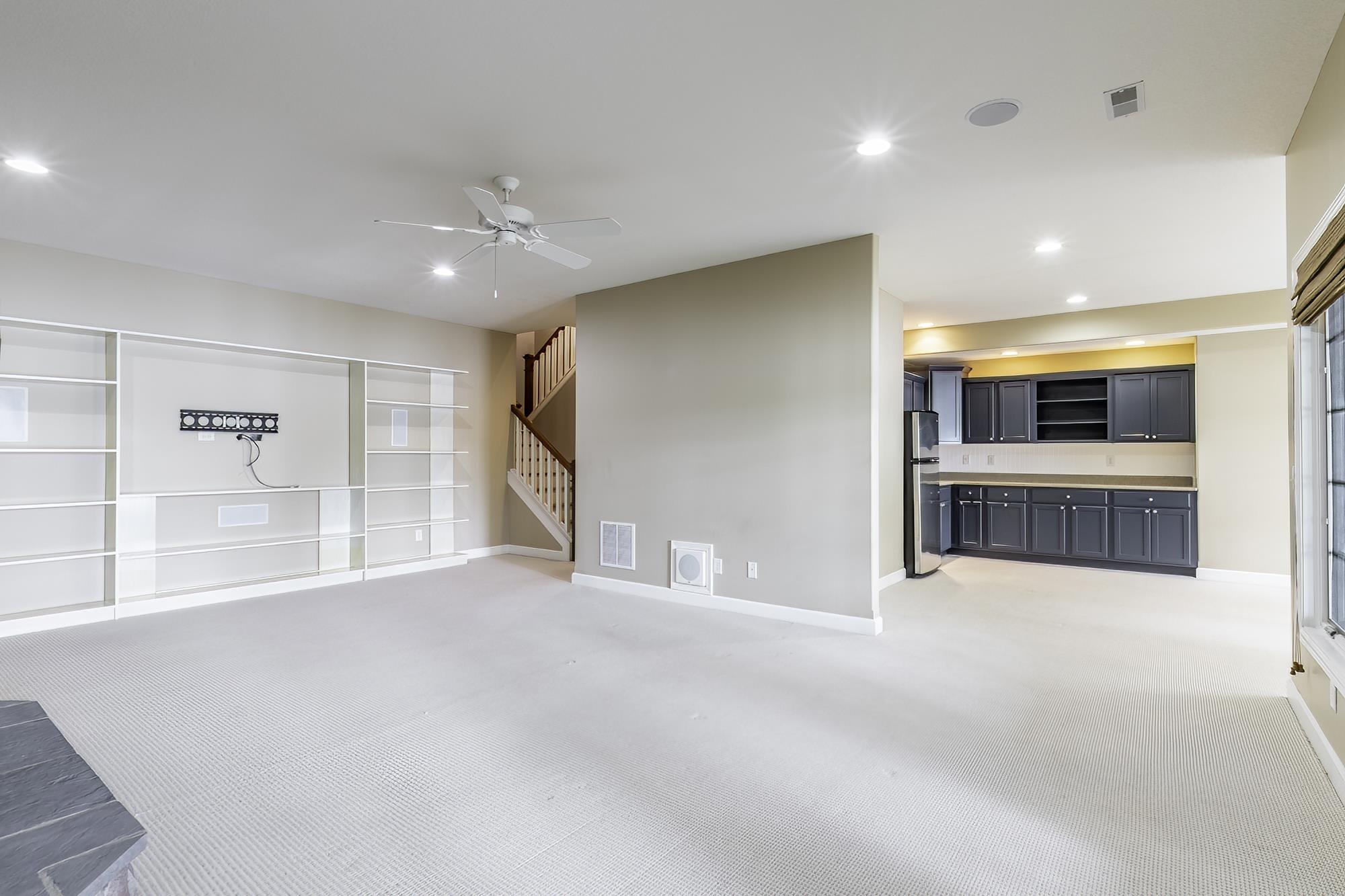 Spacious entertainment area featuring built-in shelving, recessed lighting, and ceiling fan