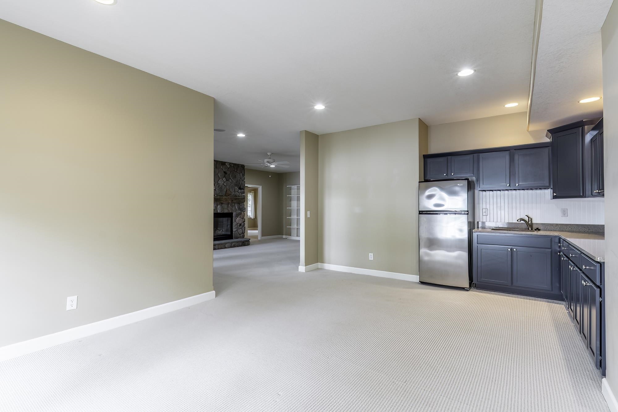 Open concept space featuring a kitchenette with dark cabinetry, stainless steel refrigerator, and stone-finish countertops