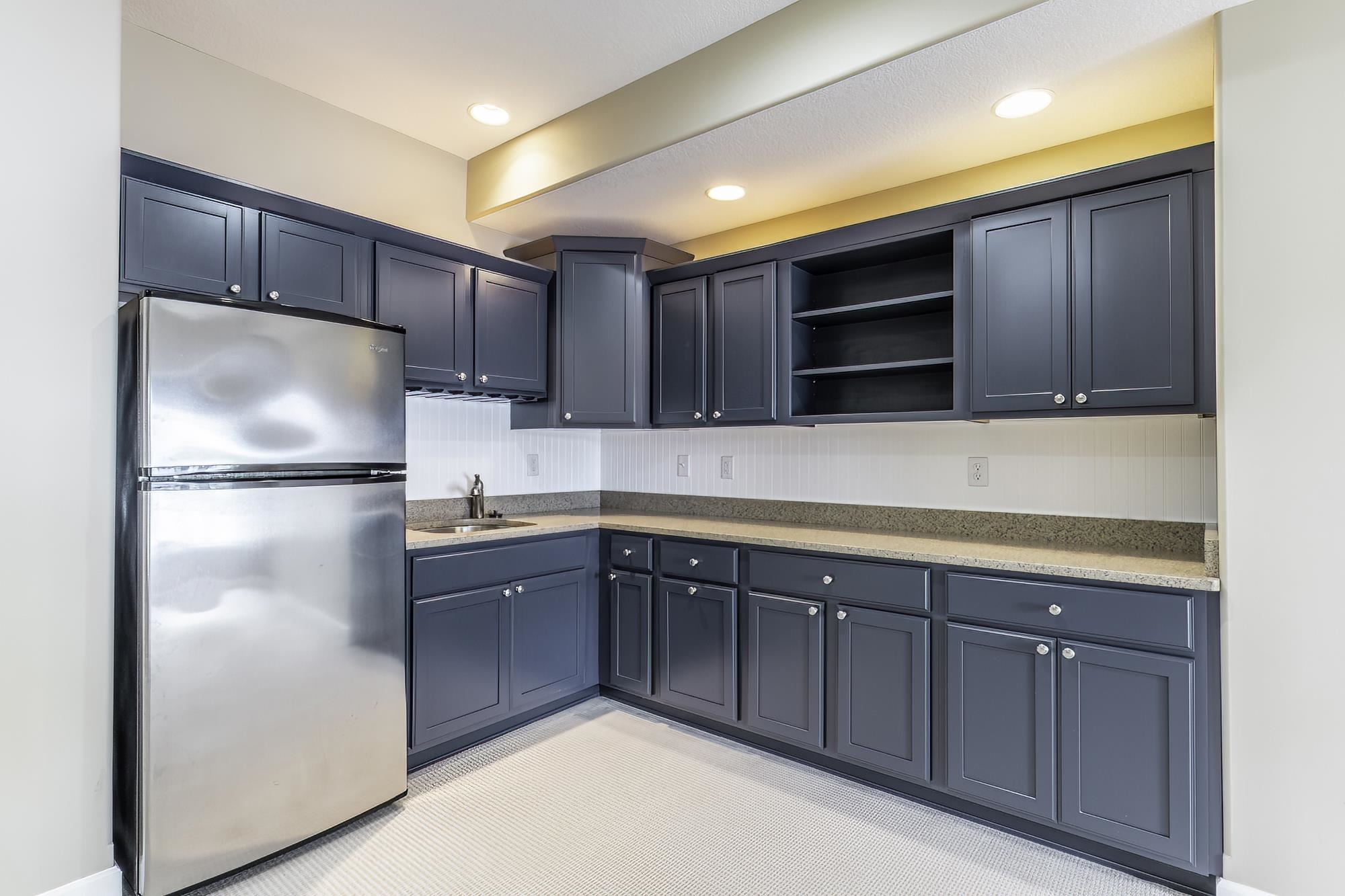 L-shaped kitchen area featuring dark gray cabinetry, light speckled countertops, a stainless steel refrigerator, and recessed lighting