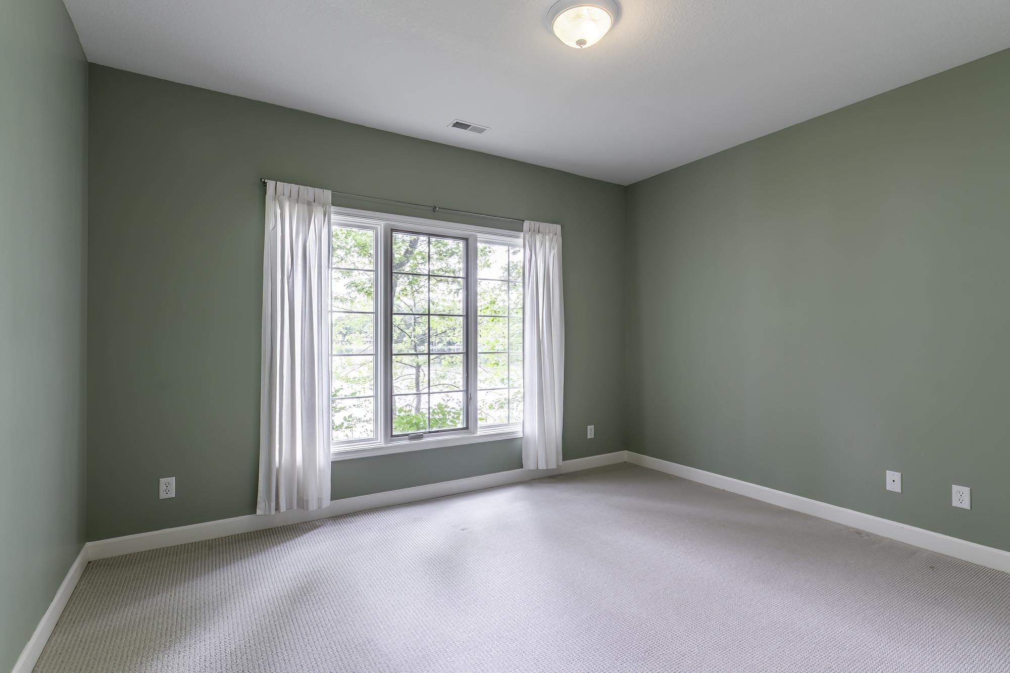 Room featuring a large bay window, light green wall paint, white trim, and light-colored carpet flooring