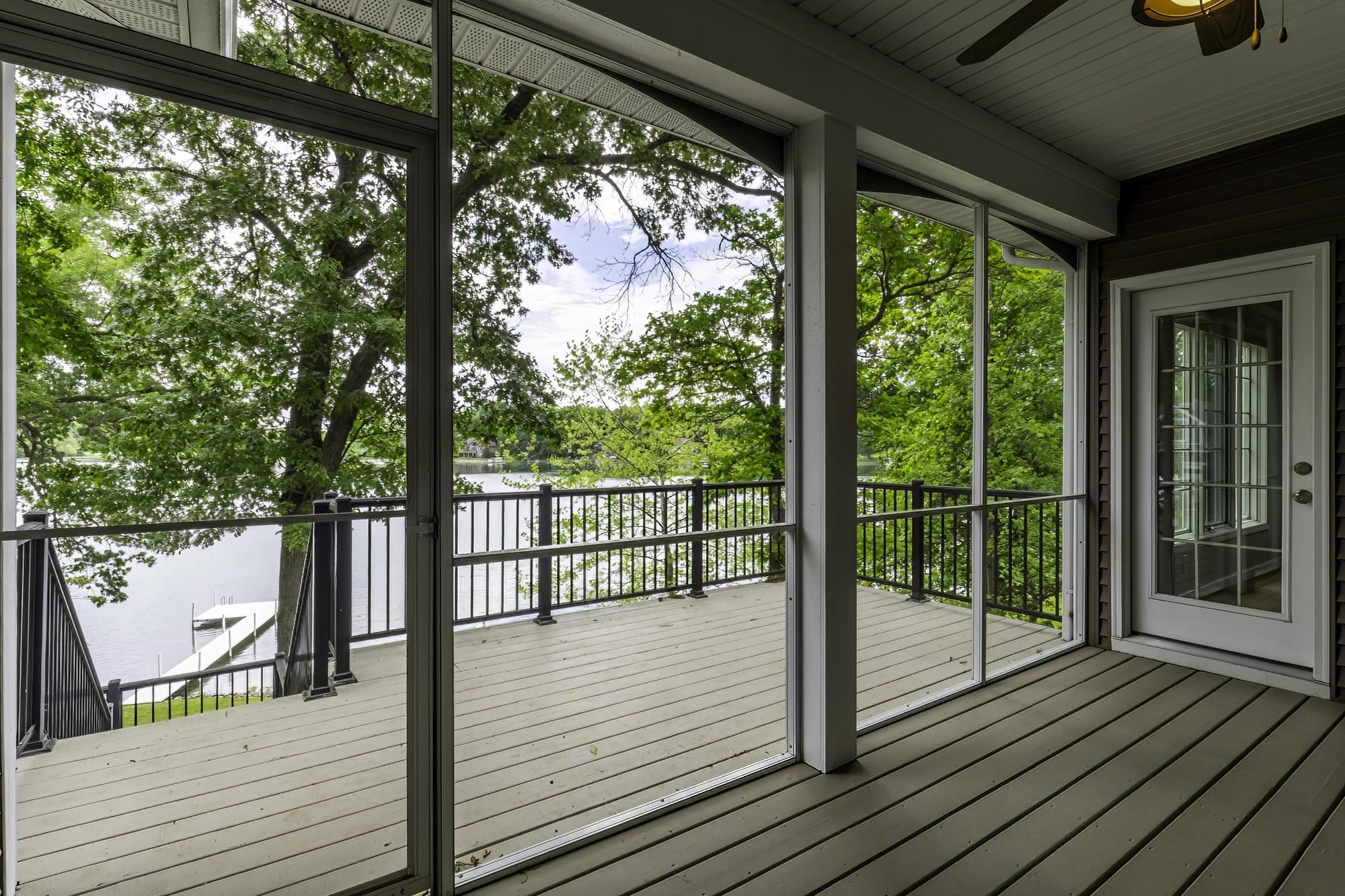 Screened porch featuring wood-finish decking, black metal railings, and a lake backdrop with a private dock