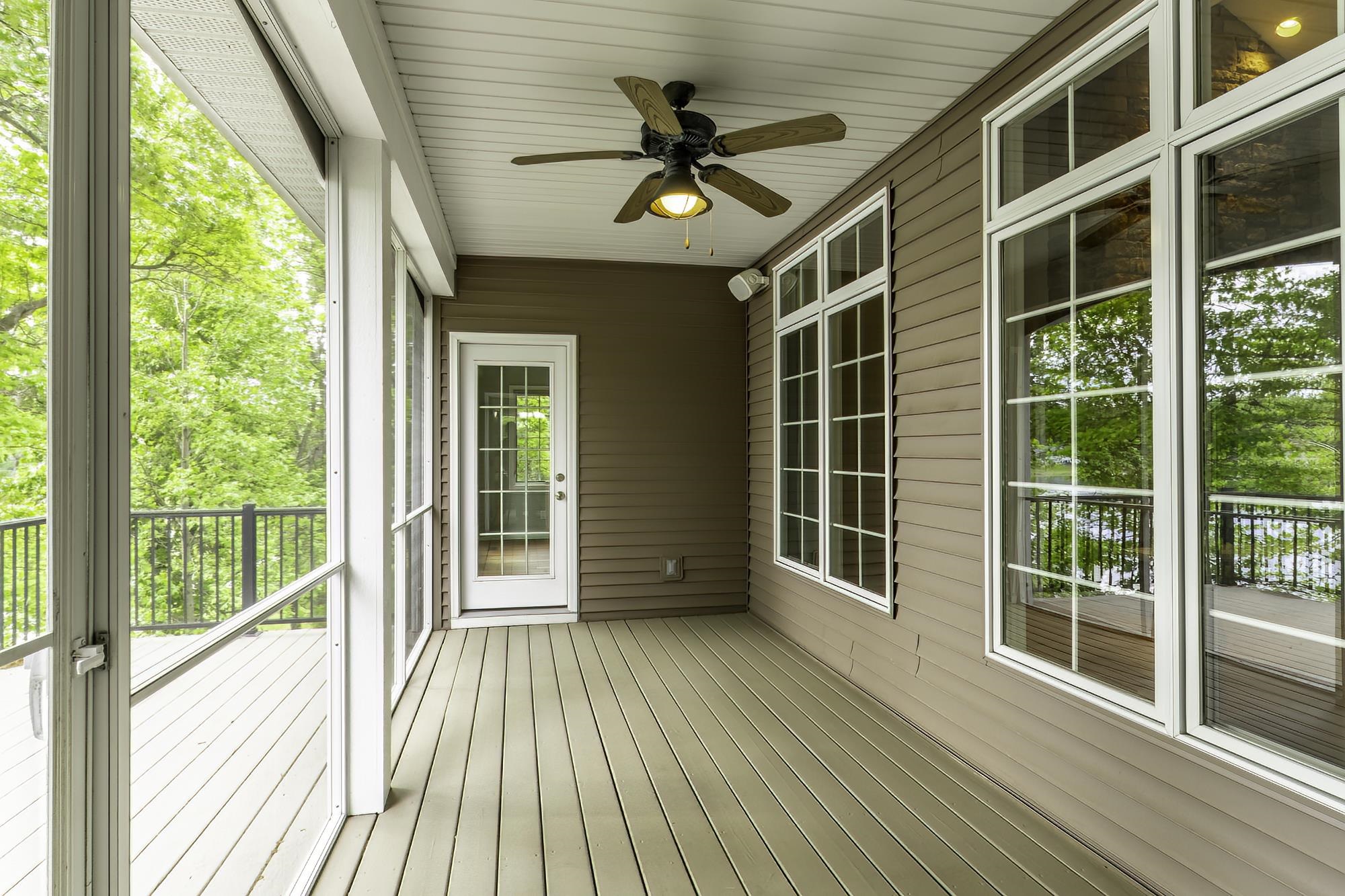 Expansive screened porch with wood-finish flooring, a ceiling fan with integrated lighting, and multiple large windows with white trim