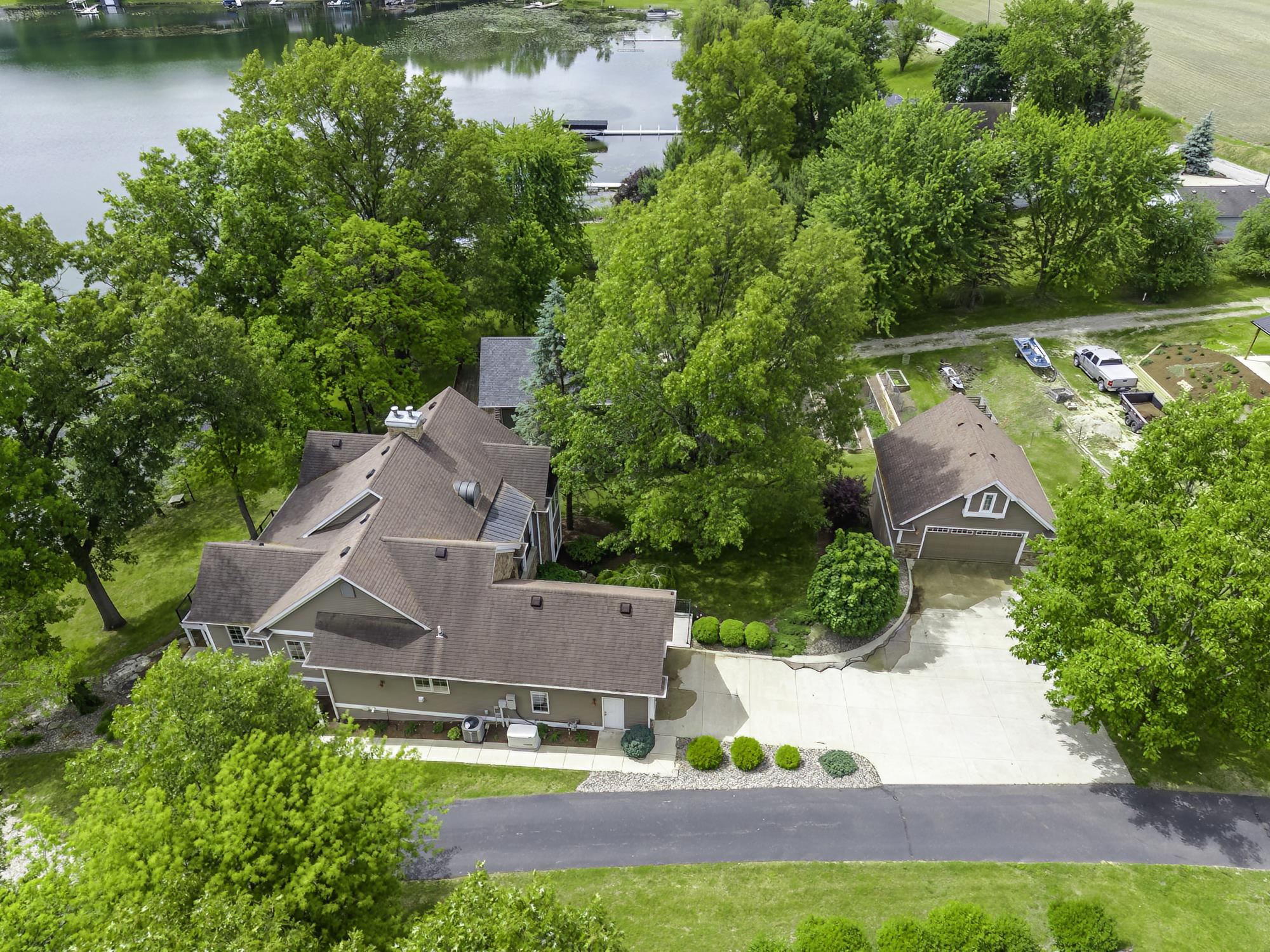Lakefront property featuring a main residence with a multi-gabled roof, an auxiliary garage structure, a private boat dock, a concrete driveway, and mature landscaping