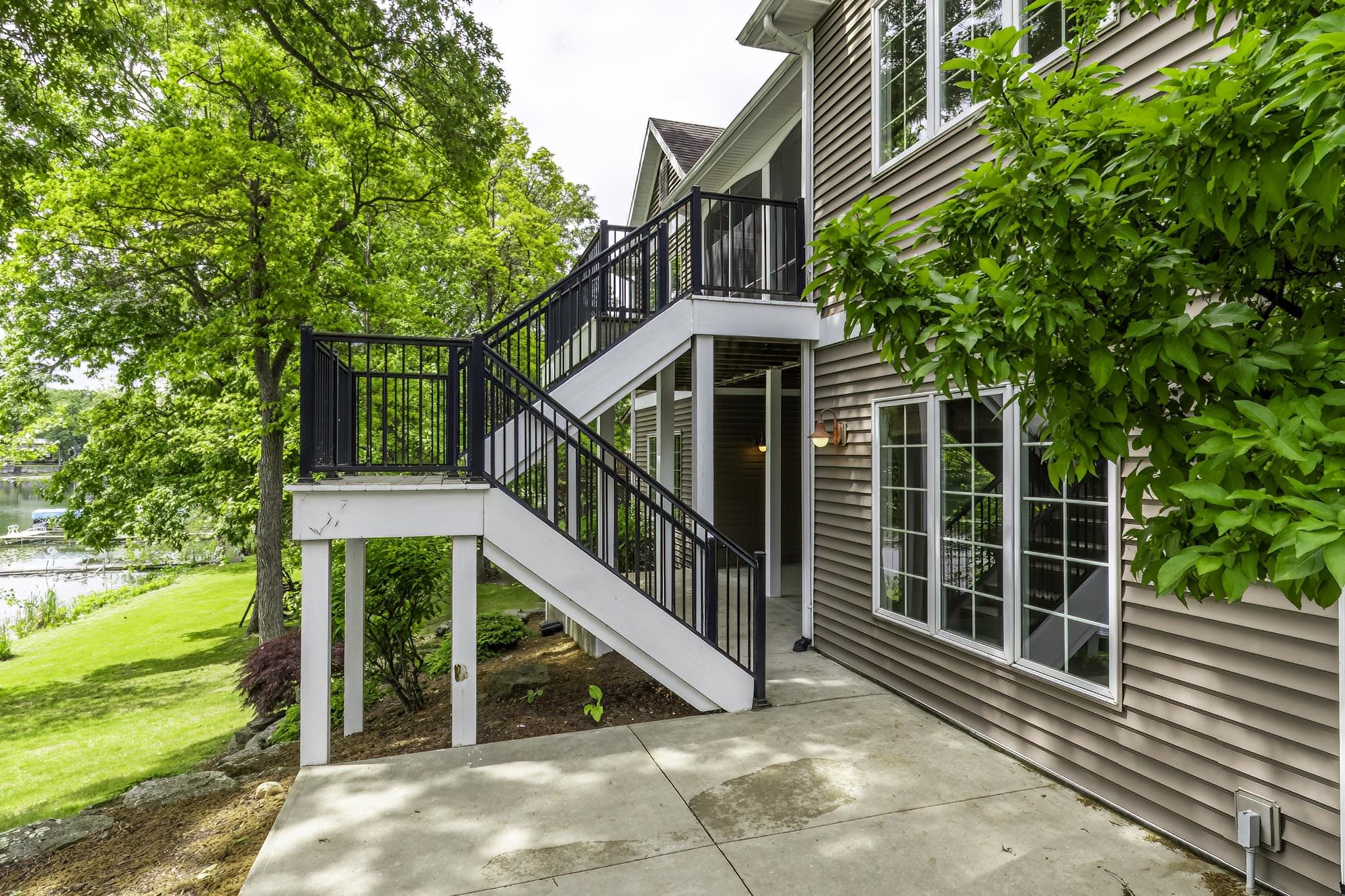Exterior siding featuring multiple windows, a concrete patio, and a staircase with black metal railings