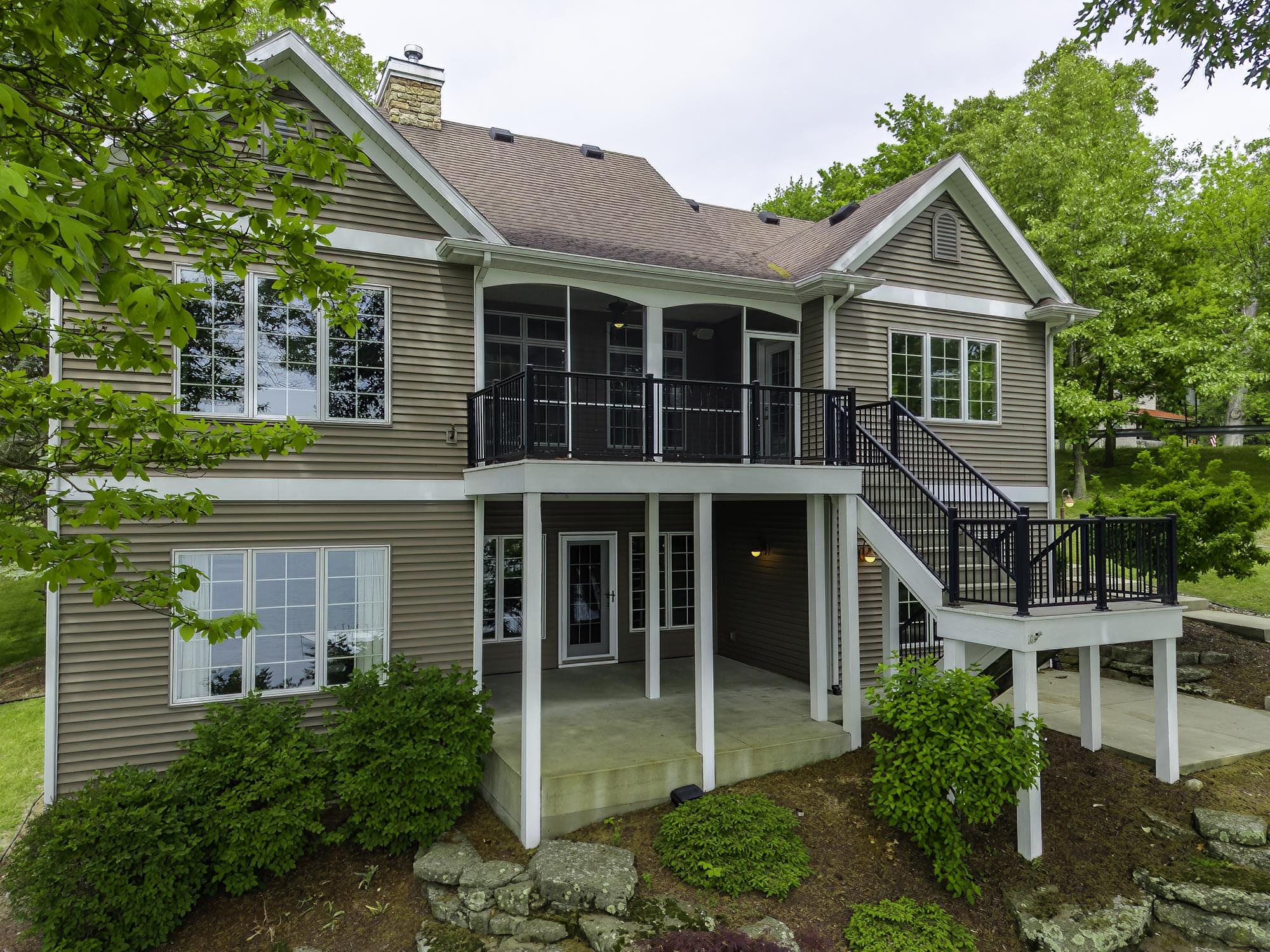 Two-story exterior with horizontal siding, multiple windows, a screened balcony, and a lower-level patio