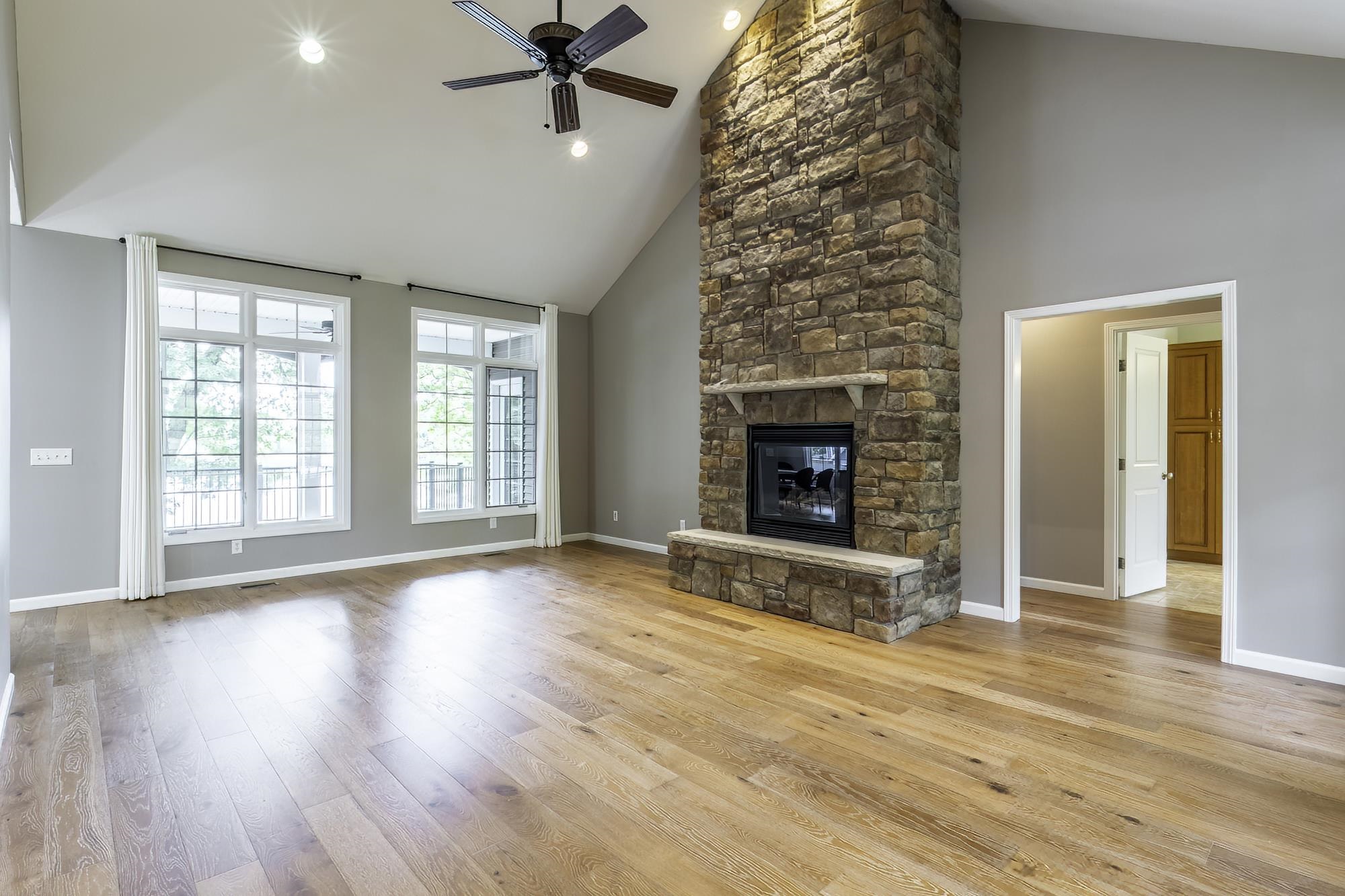 Vaulted living space featuring a floor-to-ceiling stone fireplace with a raised hearth, wood-finish flooring, and two large windows