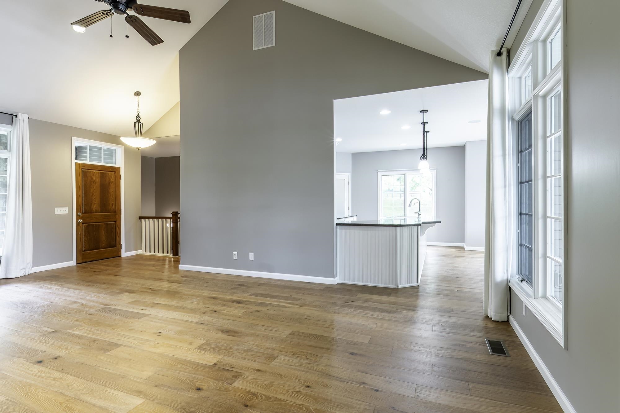 Spacious living area featuring vaulted ceilings, wood-finish flooring, and ample natural light from multi-pane windows