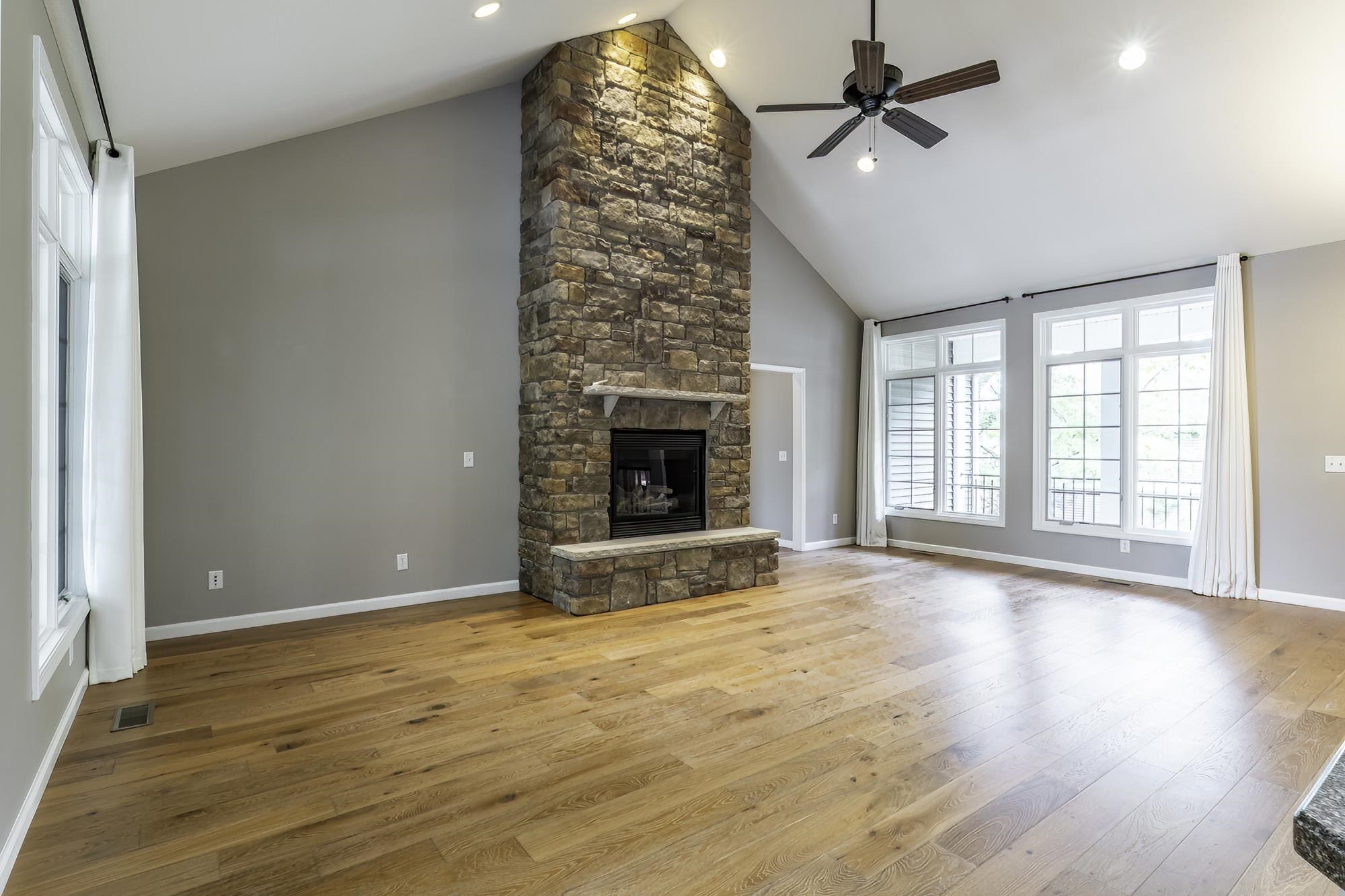 Spacious living area featuring a floor-to-ceiling stone fireplace, vaulted ceilings, and light wood-finish flooring