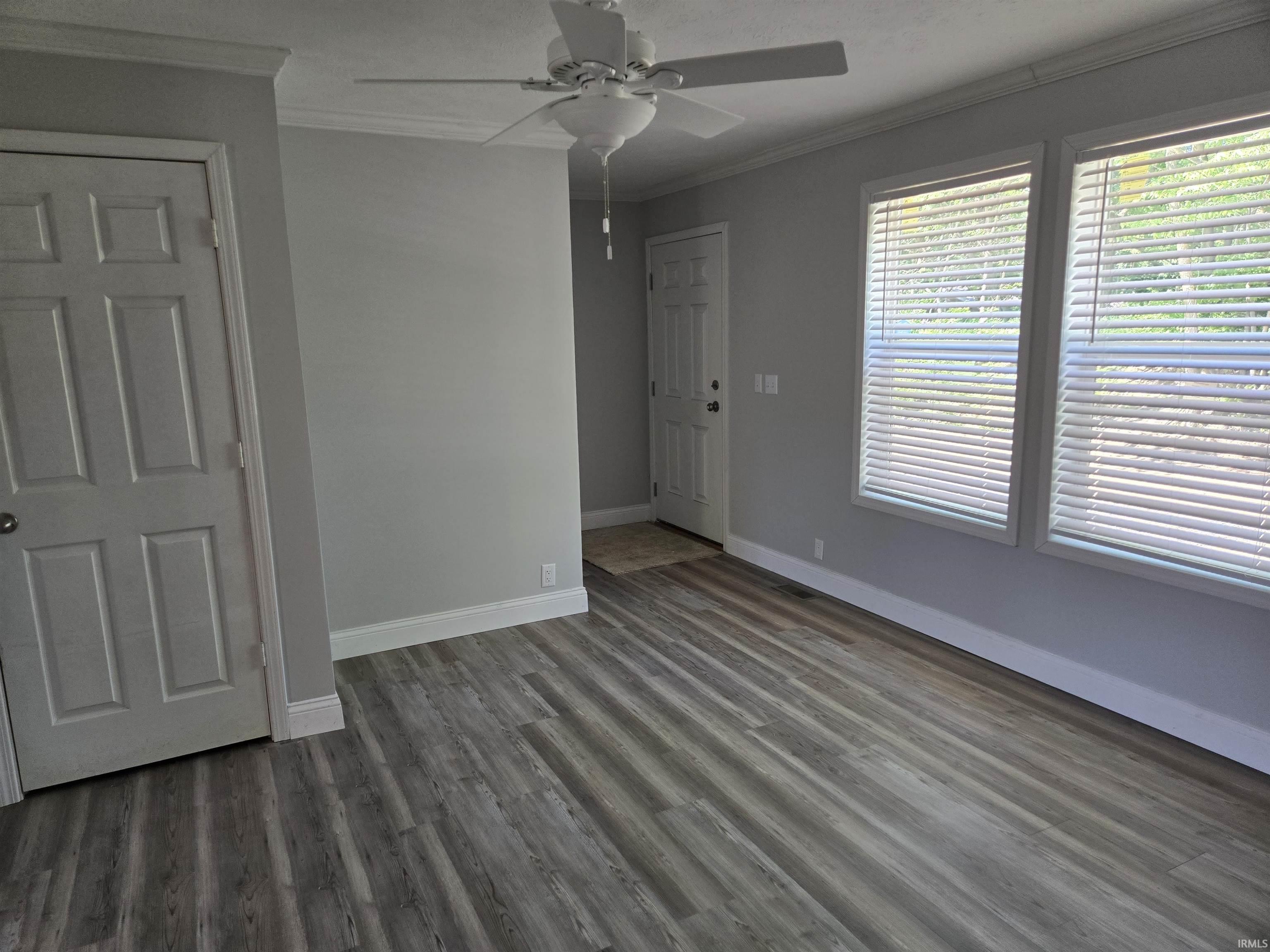 Living area featuring wood-finish flooring, two window units, and a ceiling fan