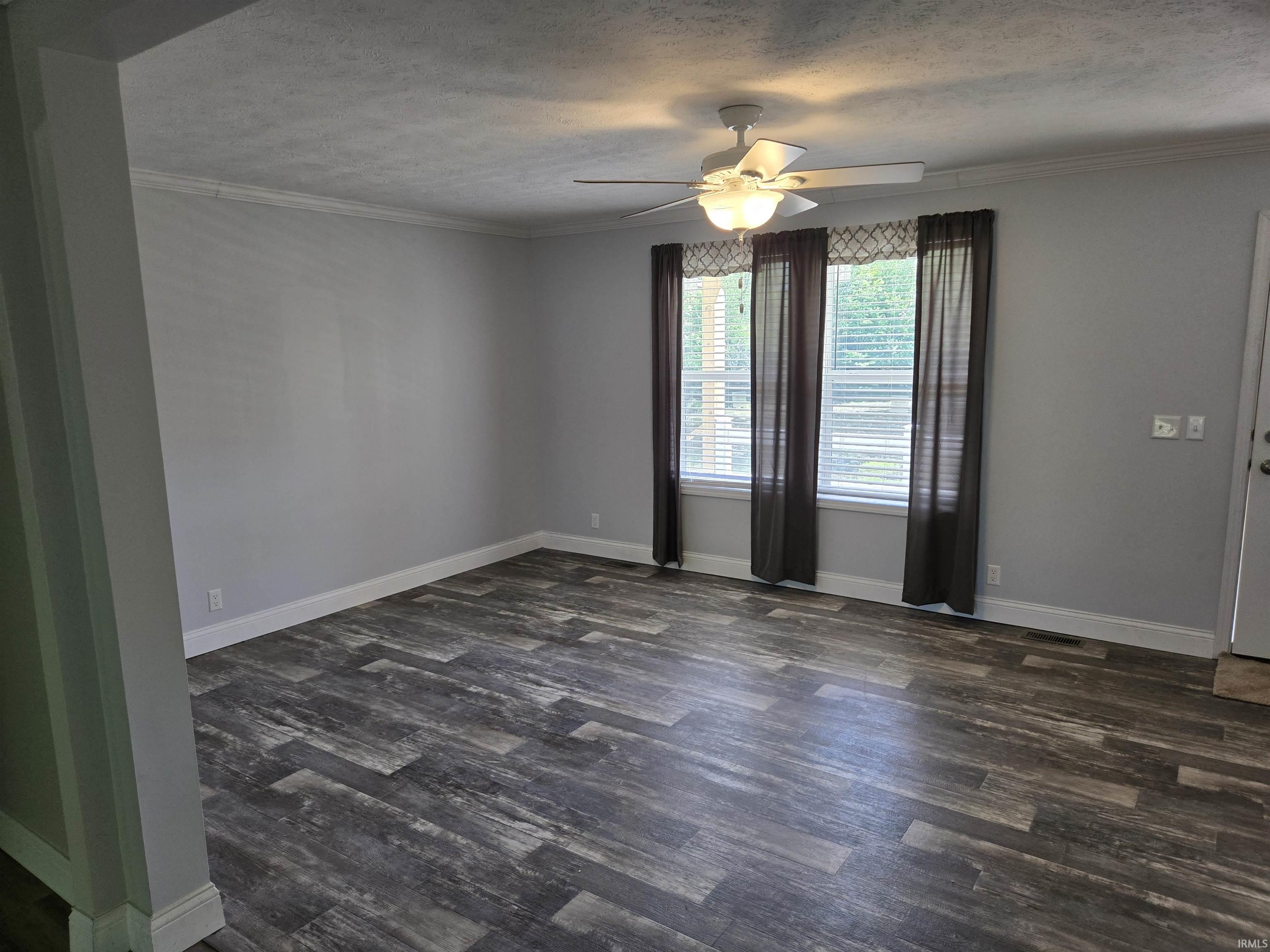 Spacious room featuring wood-finish flooring, light grey walls, and white crown molding