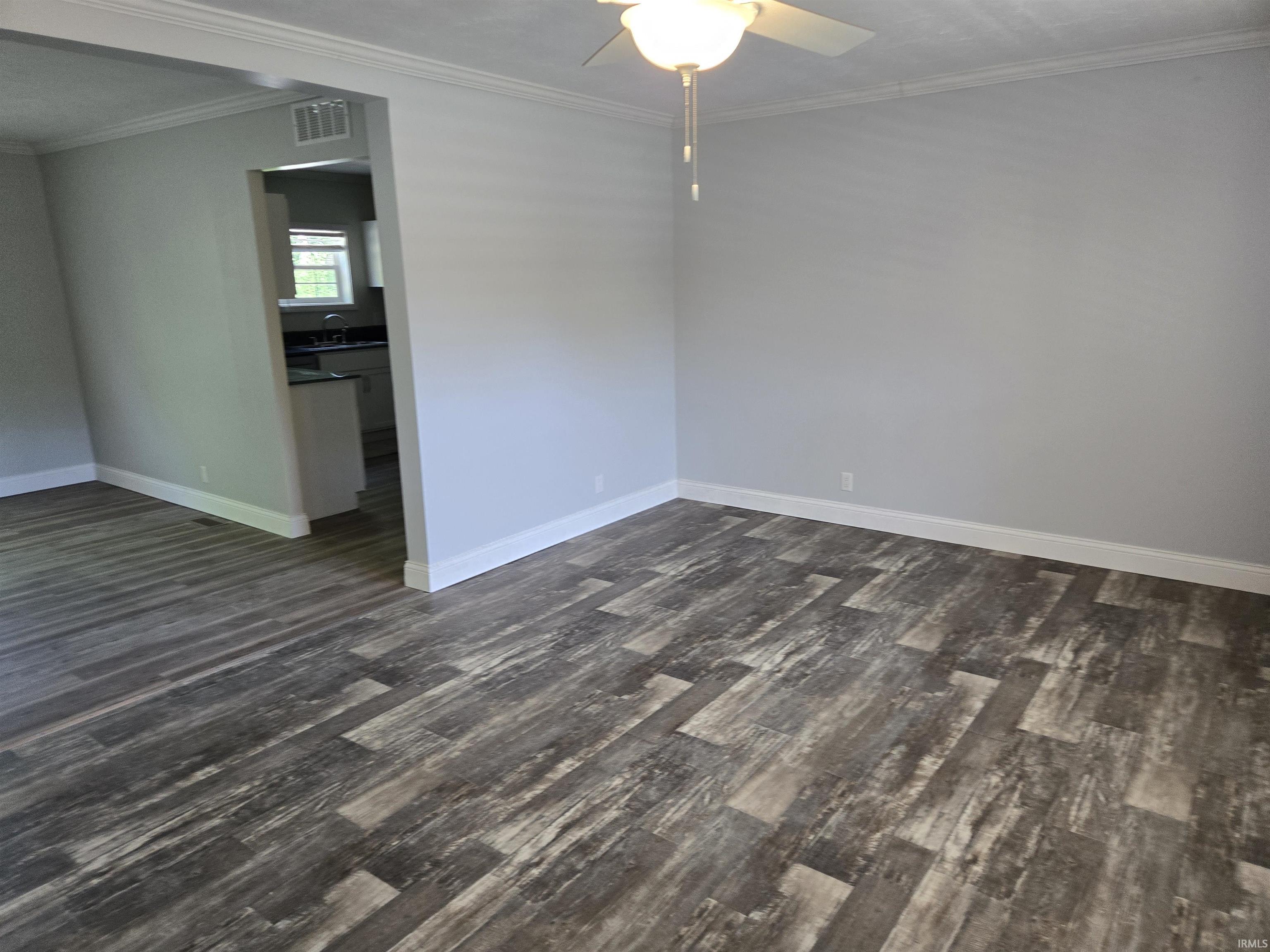 Spacious room featuring wood-finish flooring, light gray walls, white baseboards, and crown molding