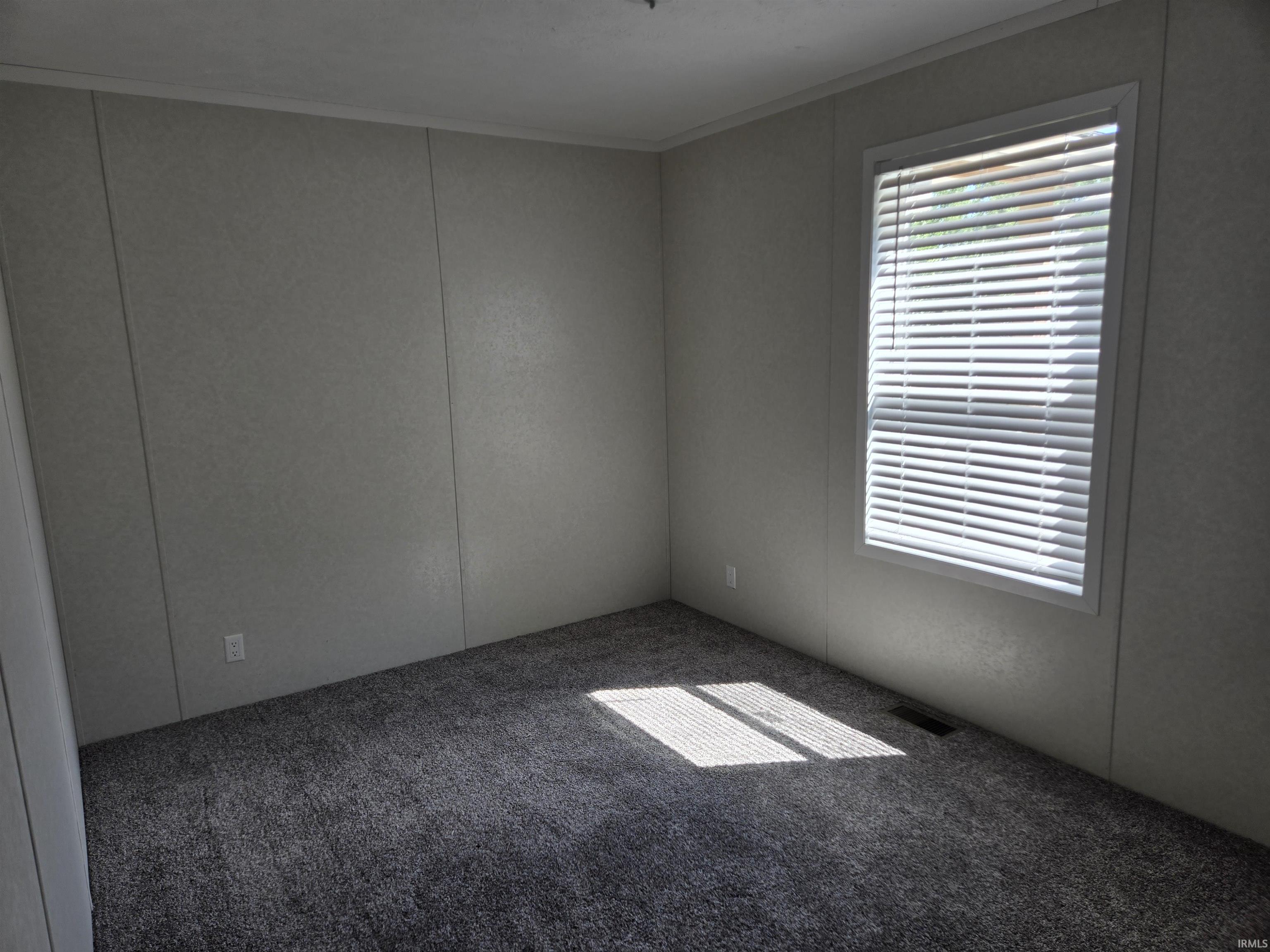 Room featuring textured wall panels, a window with white blinds, and dark patterned carpeting
