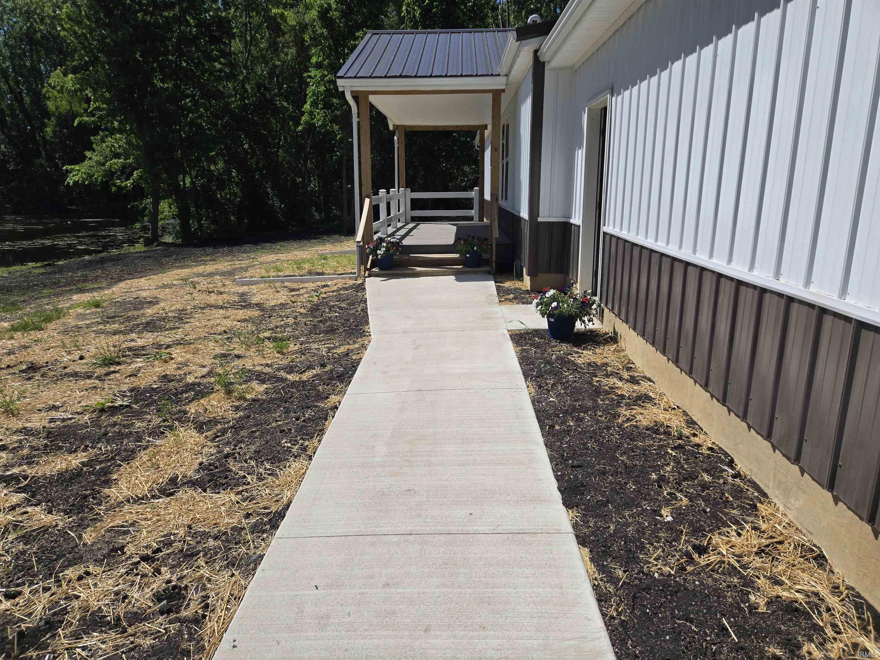 Concrete walkway leading to a covered porch with a dark metal roof
