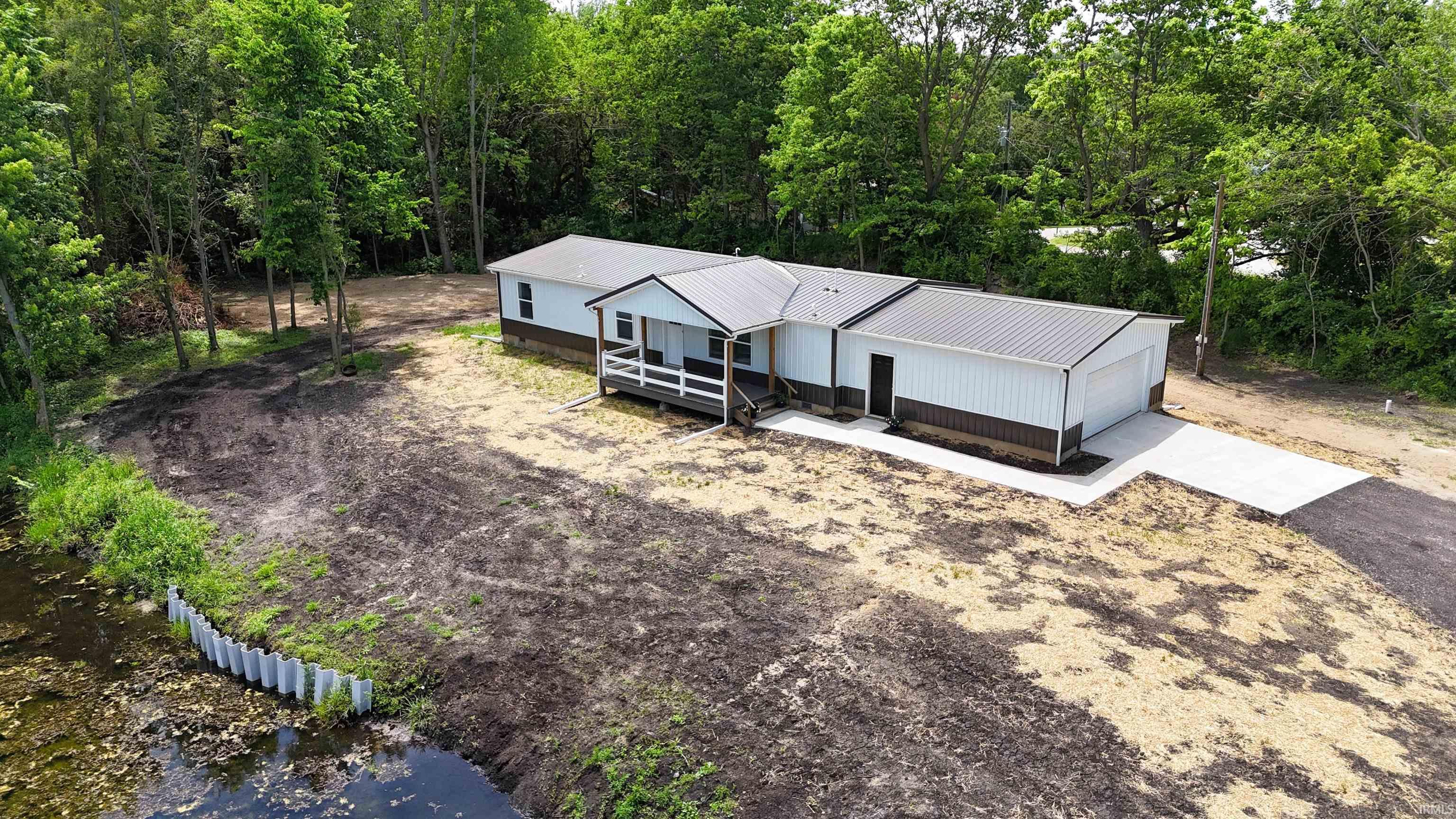 Contemporary modular home featuring a metal roof, white siding with a brown skirting, an attached two-car garage, and a concrete driveway