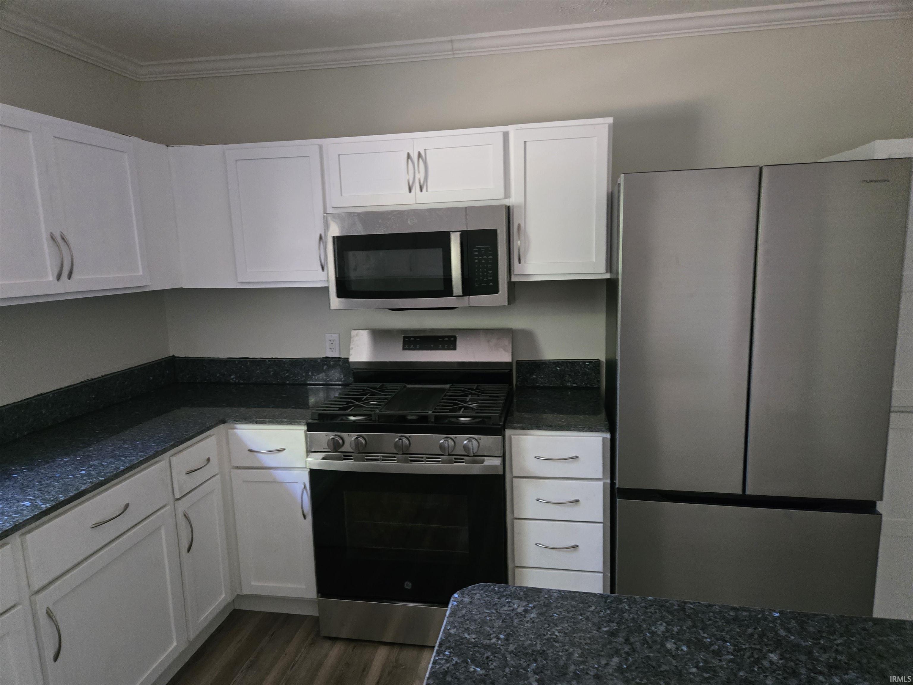Kitchen featuring white shaker-style cabinetry, dark speckled countertops, and stainless steel appliances