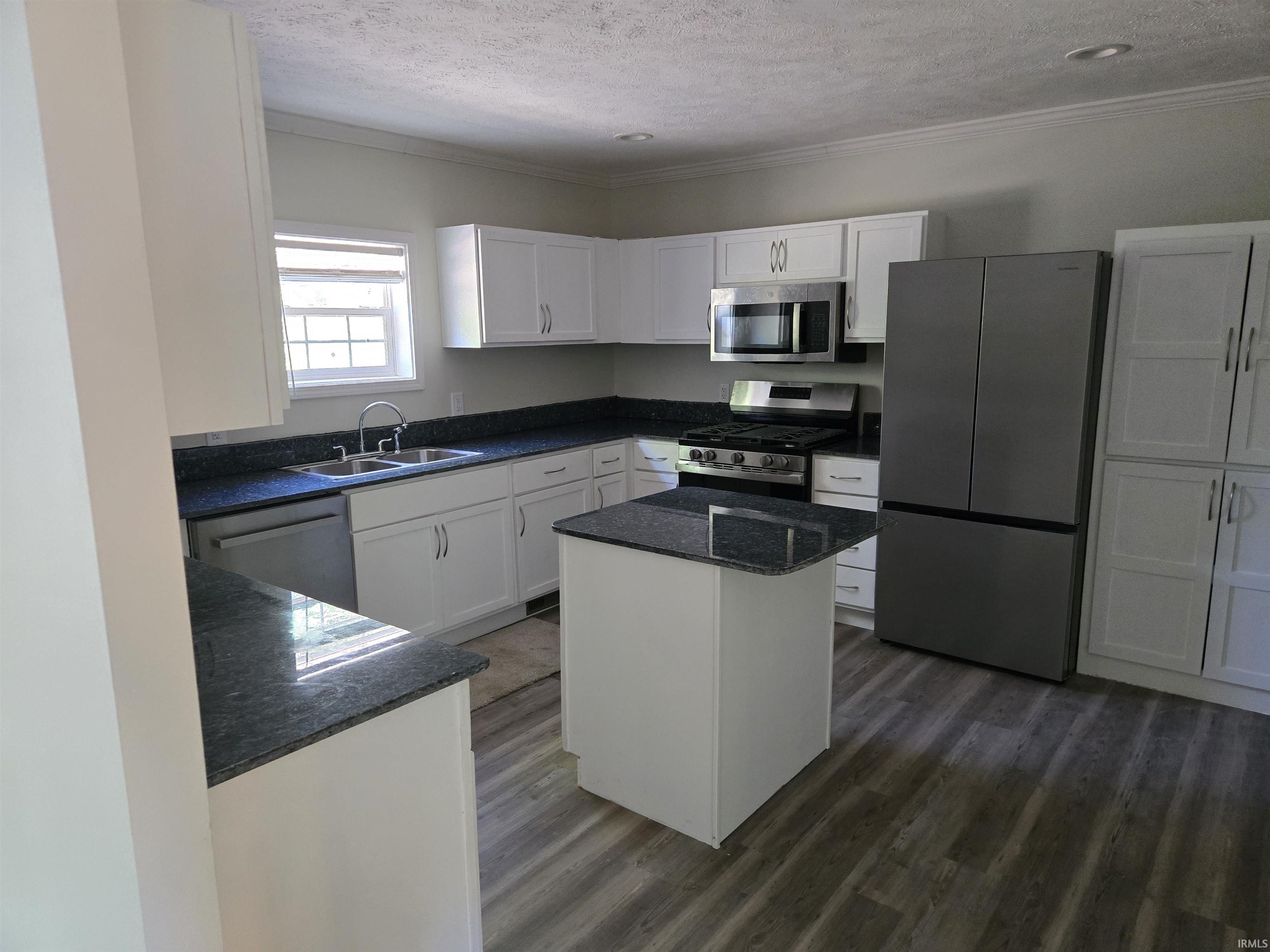 Modern kitchen featuring white cabinetry, dark countertops, a central island, stainless steel appliances, and wood-finish flooring