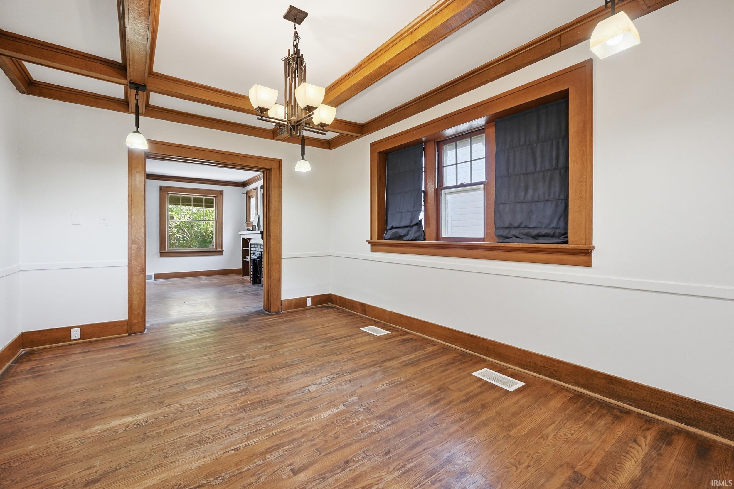 Room featuring wood-finish flooring, exposed wood ceiling beams, a decorative chandelier, and a wide cased opening