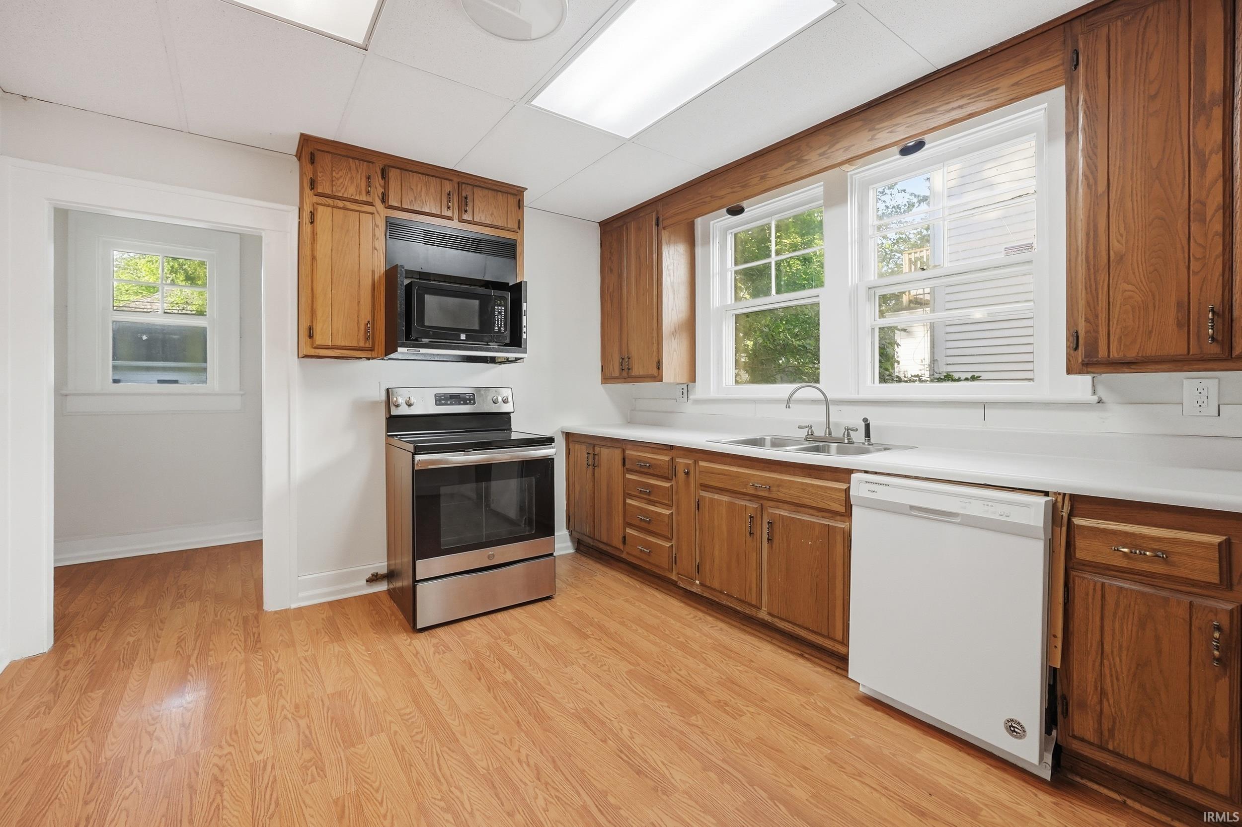 Kitchen featuring wood-finish flooring, oak cabinetry, white countertops, and white appliances