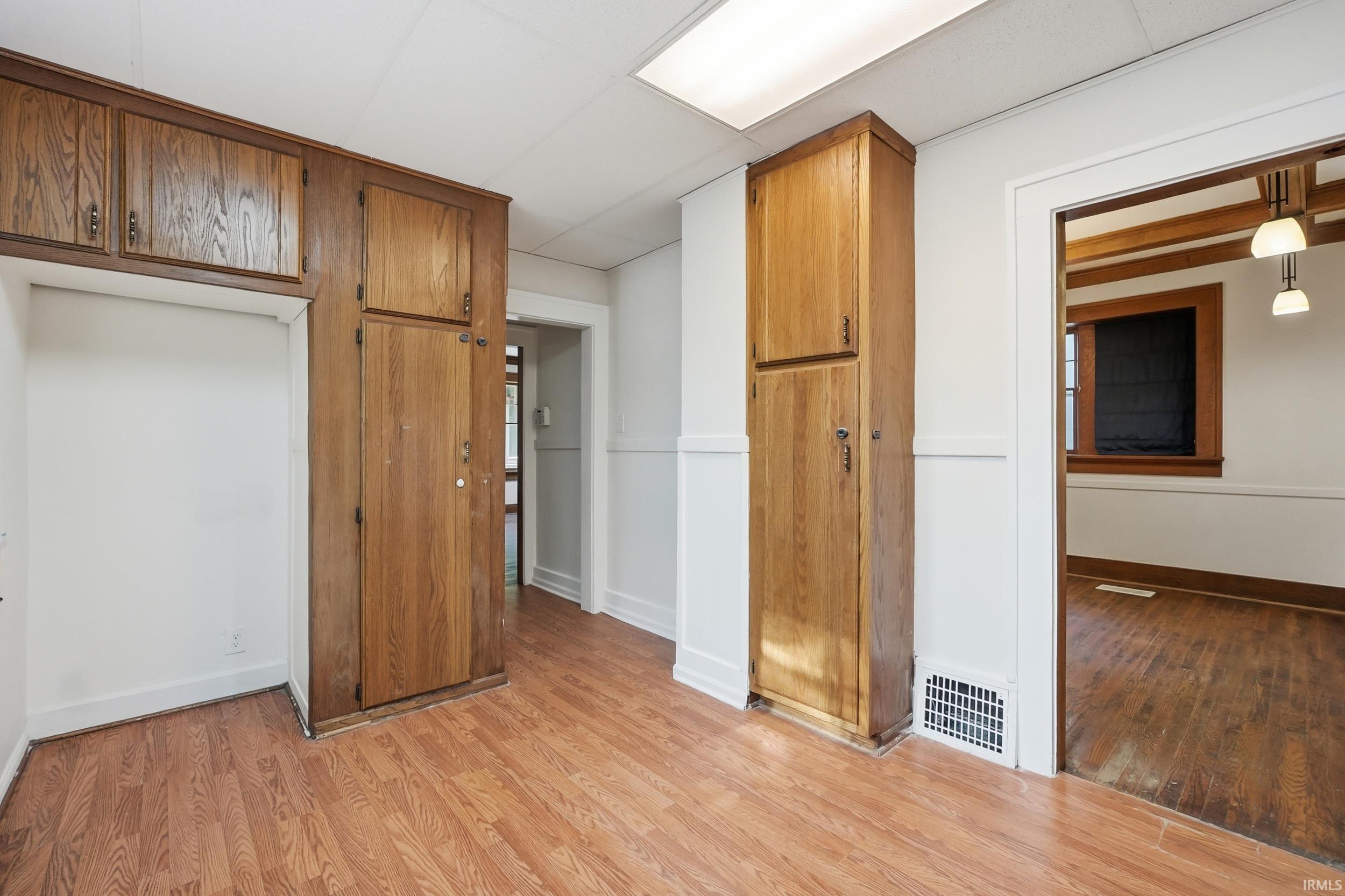 Wood-finish flooring throughout, featuring a built-in pantry with wood cabinetry, additional overhead wood storage, and a dedicated alcove