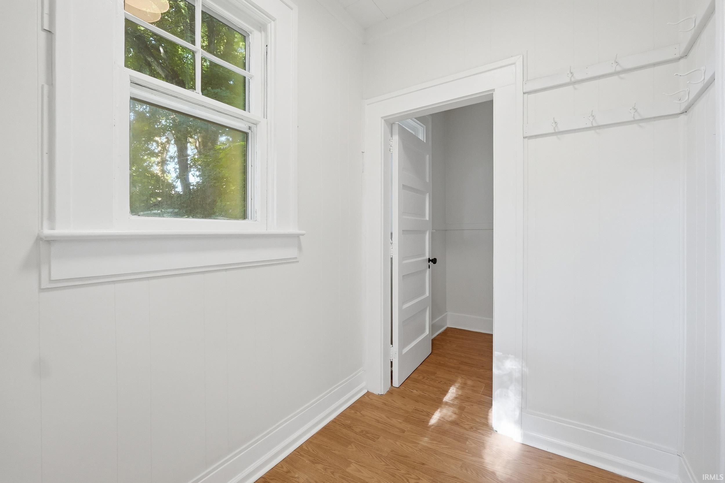 Room featuring wood-finish flooring, white paneled walls, and a multi-pane window with white trim