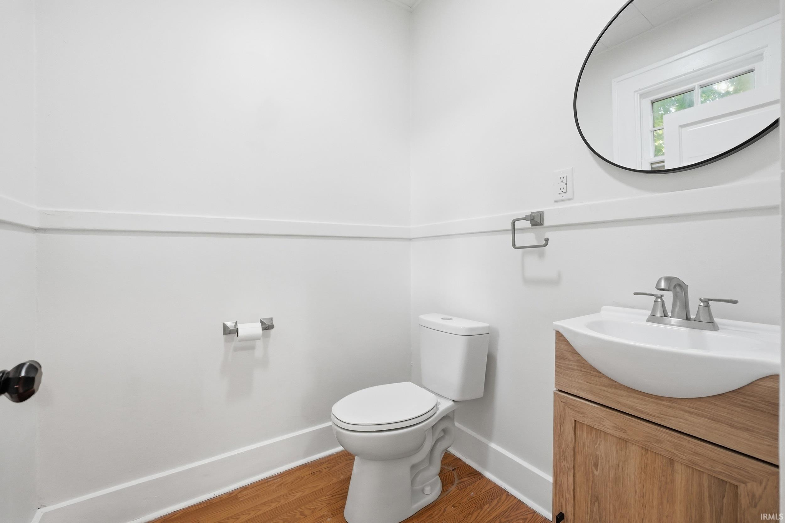 Compact bath featuring a wood-finish vanity with an integrated white sink, brushed nickel faucet, and a contemporary round mirror