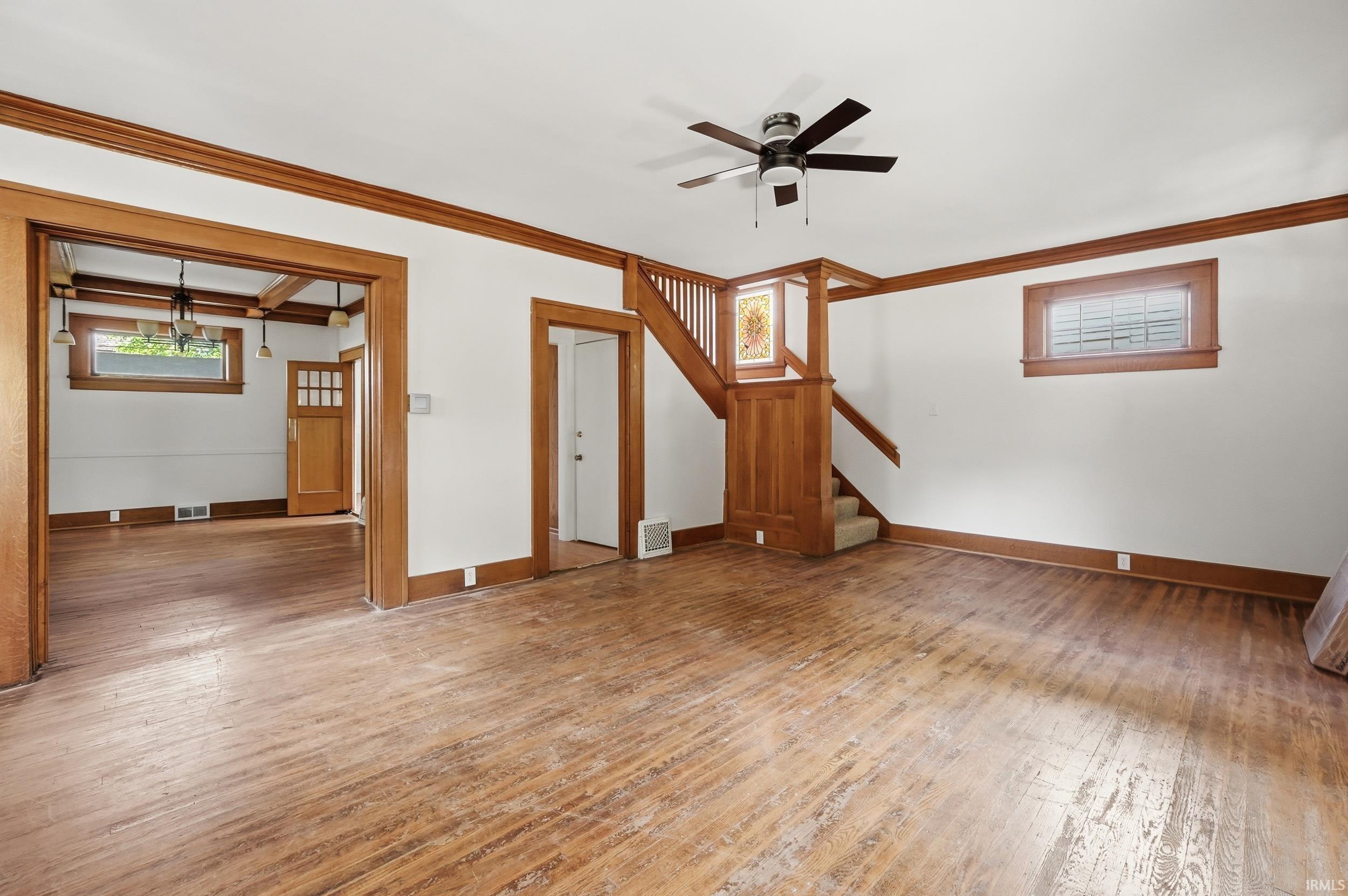 Expansive interior space featuring wood-finish flooring, extensive wood trim, a built-in staircase with decorative stained glass, and a ceiling fan with integrated lighting