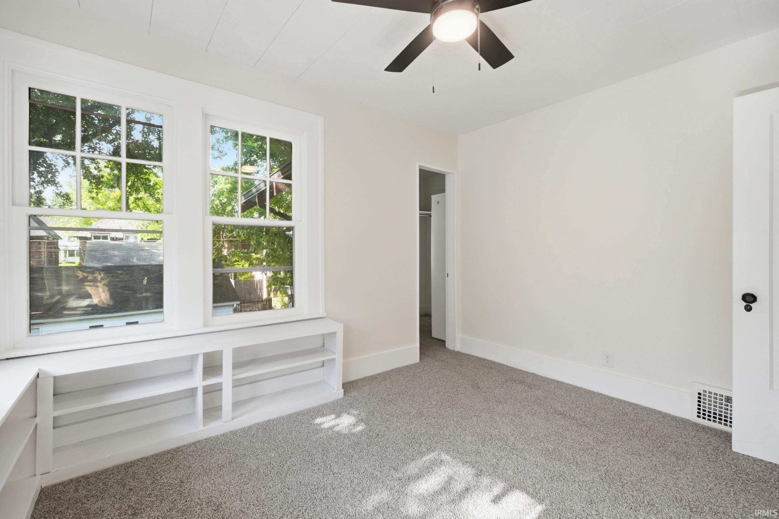 Bright room featuring two large windows, built-in shelving, a ceiling fan, and light gray carpet flooring