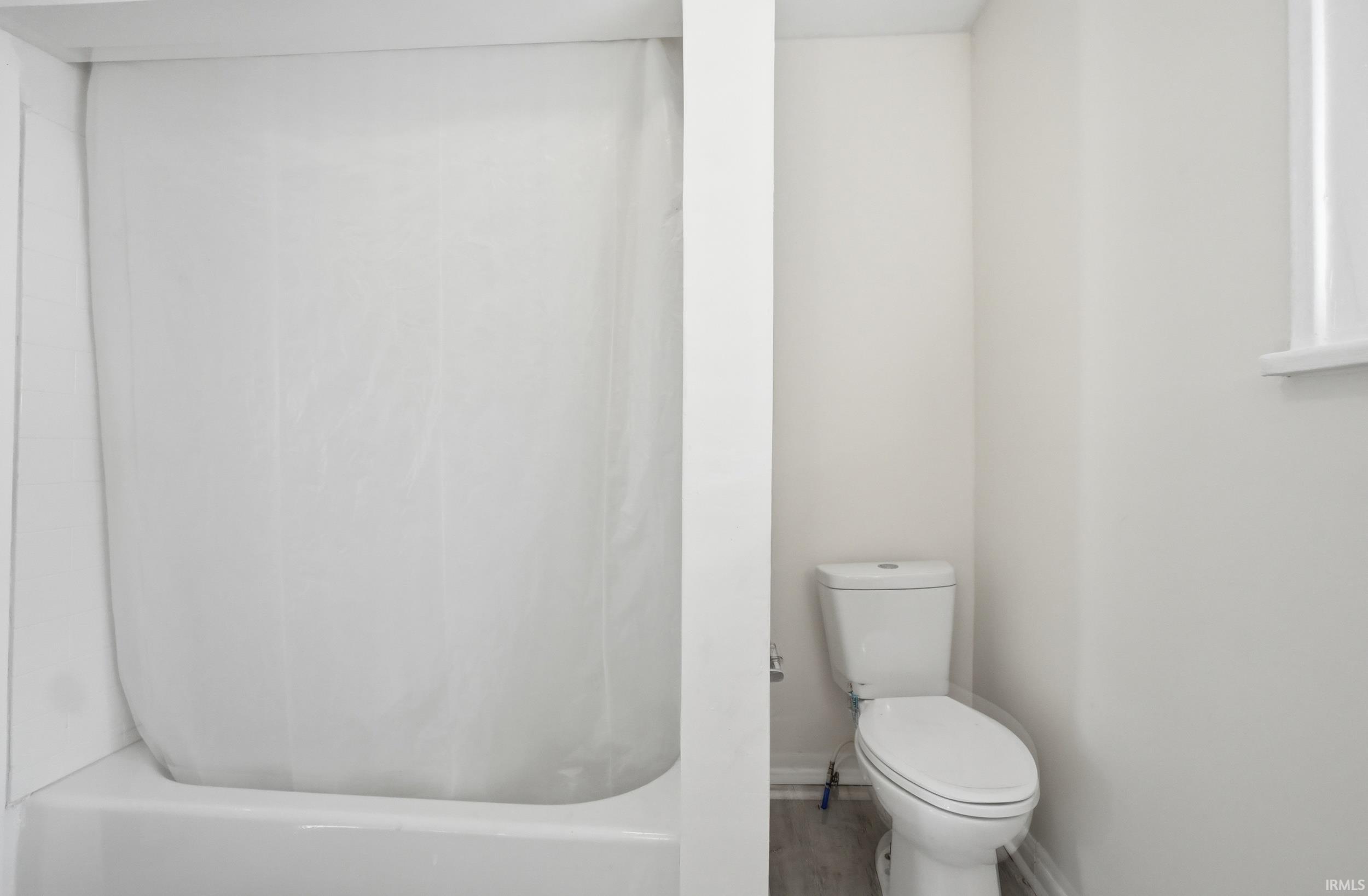 Bathroom featuring a white tub/shower combination, white walls, and wood-finish flooring