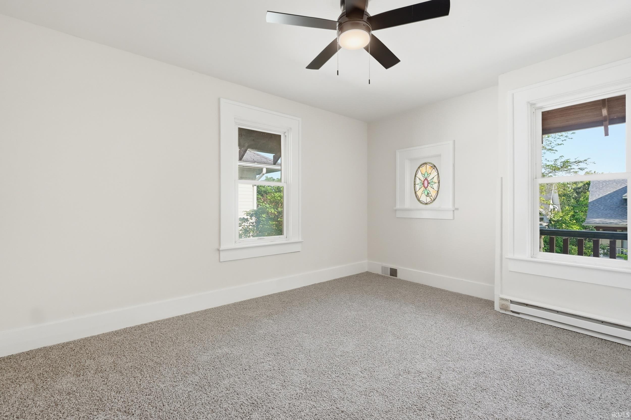 Carpeted room with white walls, a ceiling fan, and two windows
