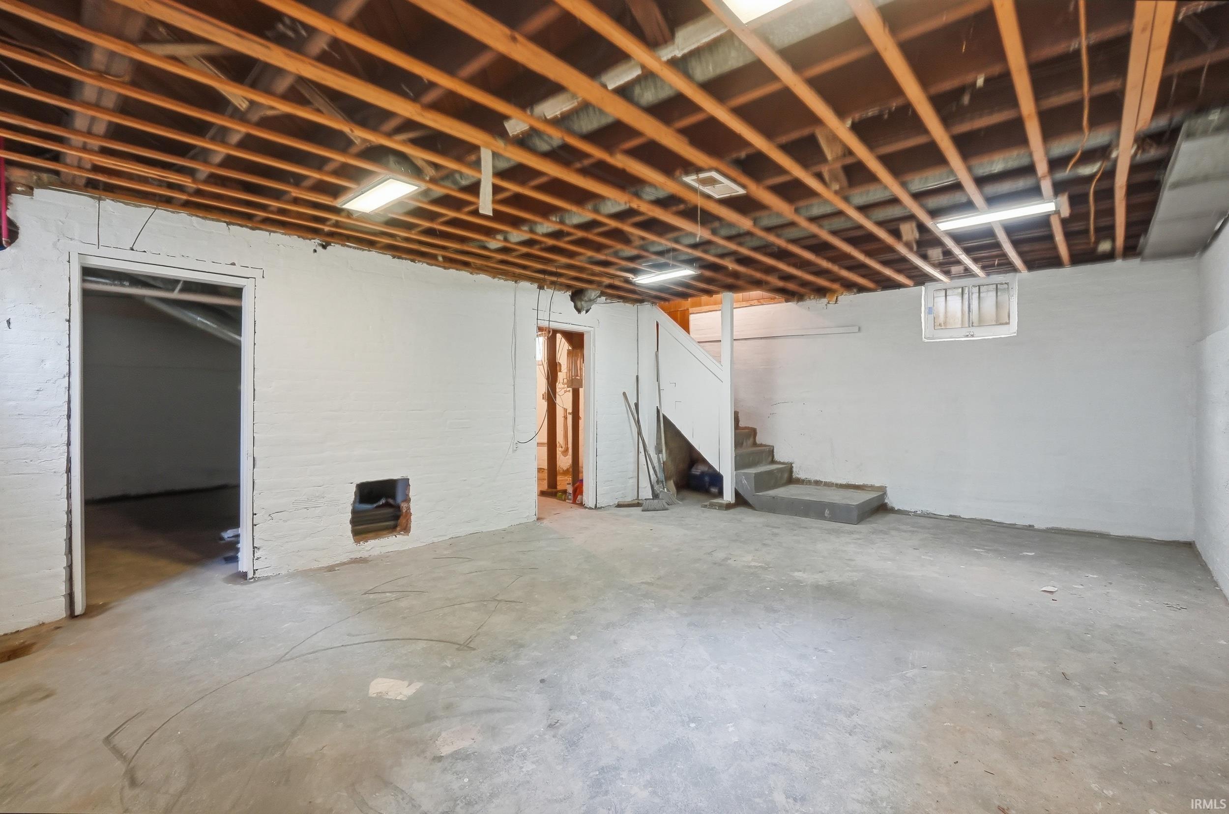 Unfinished basement offering exposed ceiling joists, concrete flooring, painted block walls, and a visible staircase