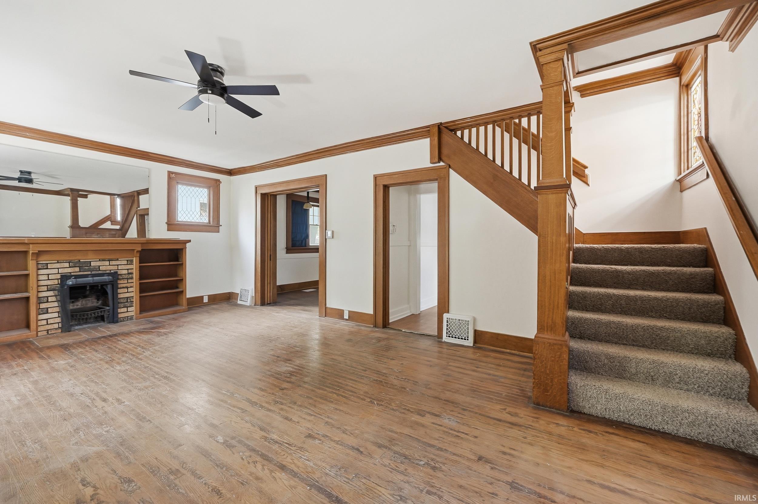 Spacious room featuring wood-finish flooring, a brick fireplace with built-in shelving, and a ceiling fan