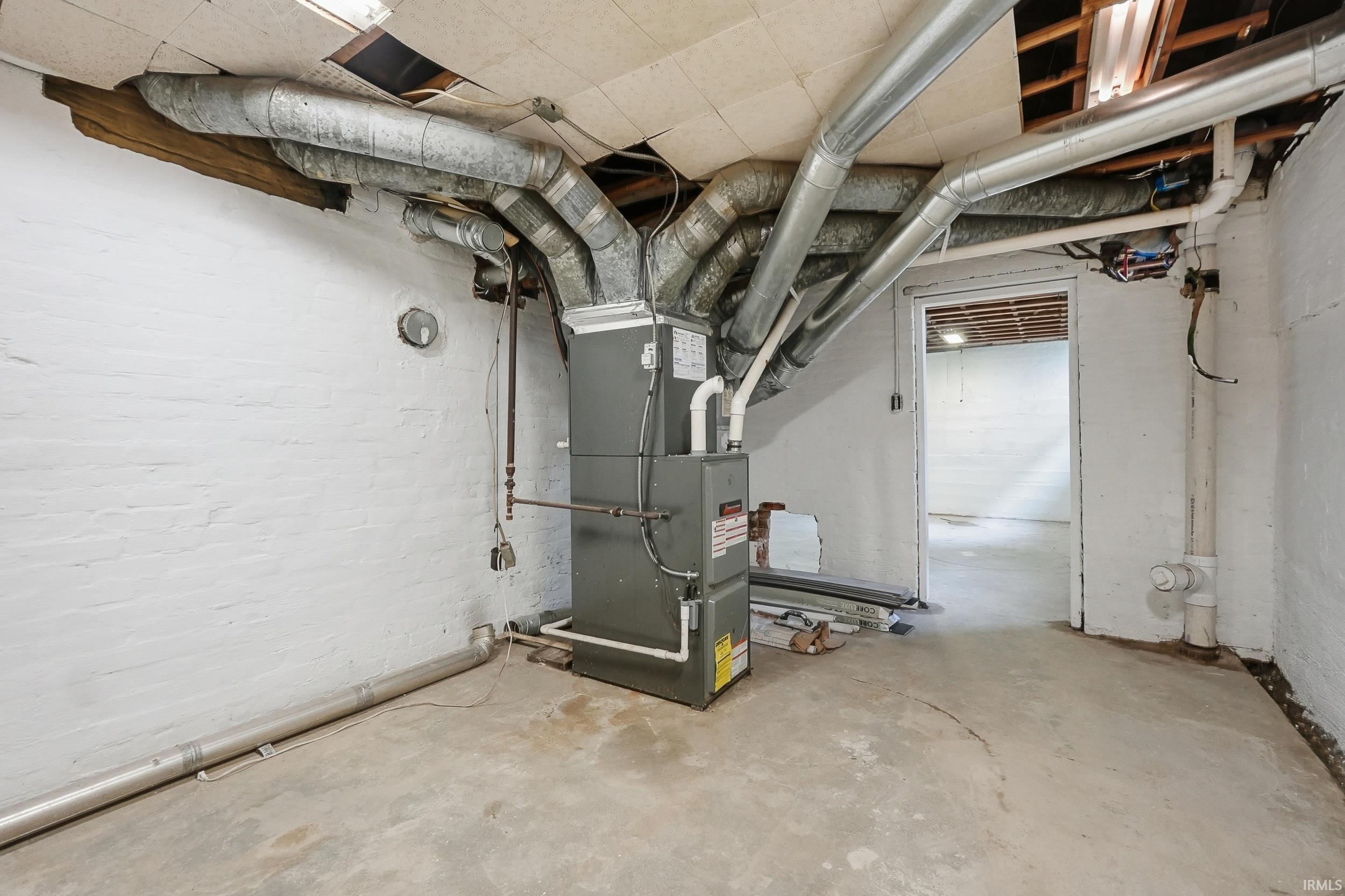 Basement space featuring exposed ceiling joists and ductwork, a central forced-air unit, and painted cinder block walls